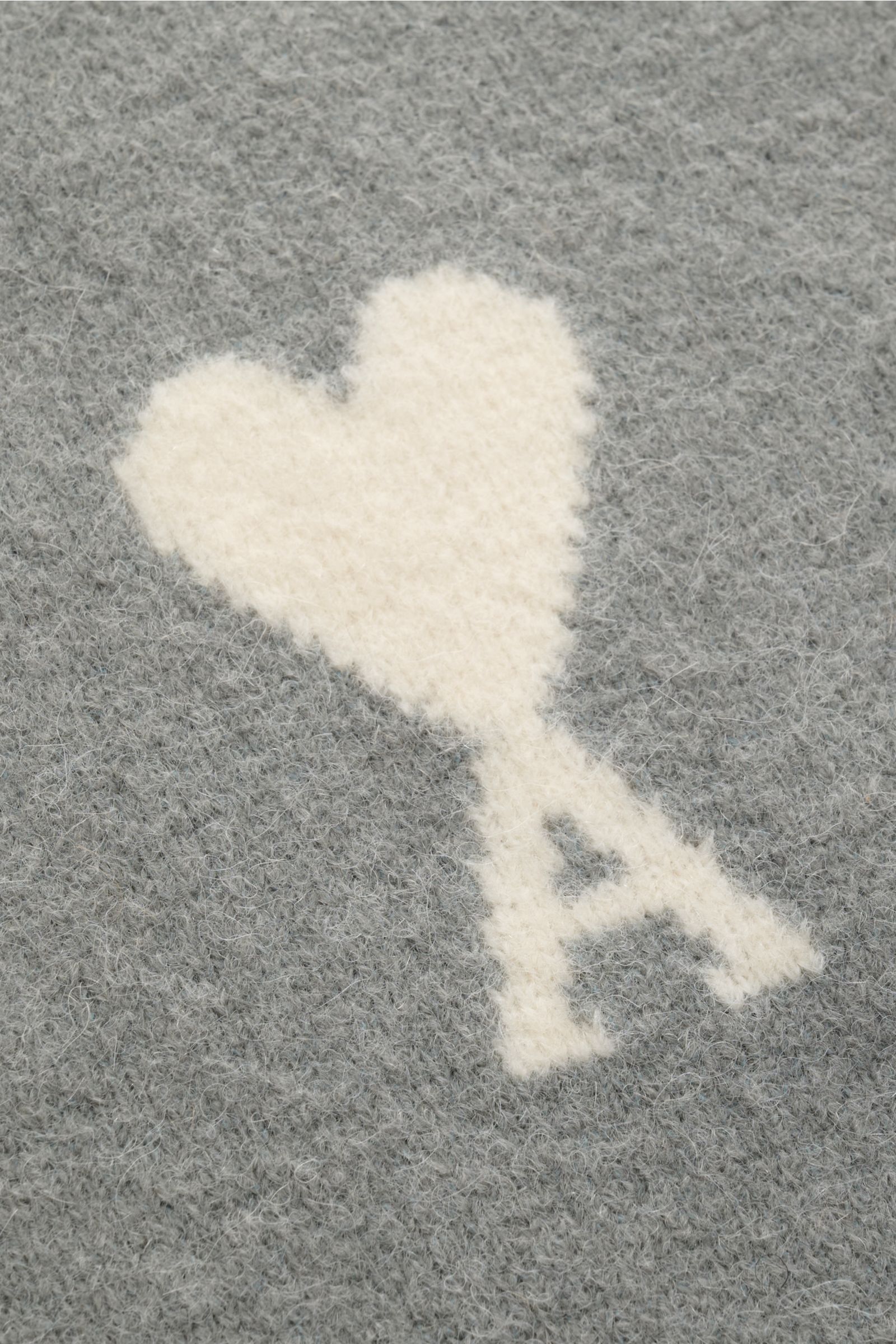 Nahaufnahme des eingestrickten weißen Herz-Logos auf dem weichen, grauen Ami Paris Cardigan grau aus Alpakawoll-Mischung.