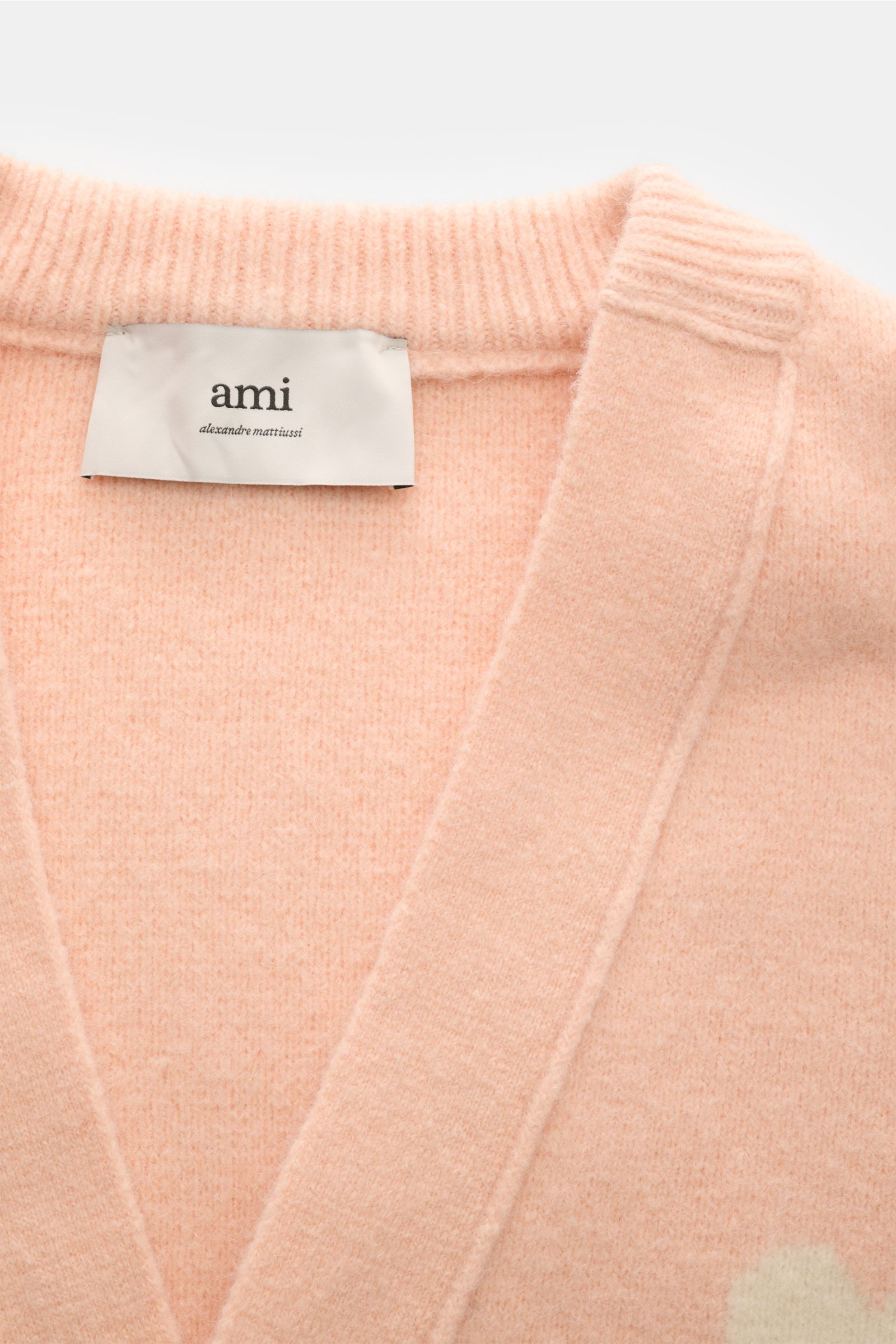 Close-up front view of the Ami Paris Cardigan rosé showing the soft, voluminous alpaca blend knit with V-neck, ribbed collar, and logo label inside the collar. Legerer Luxus für kalte Tage: AMI PARIS interpretiert seinen ikonischen Cardigan mit großem 