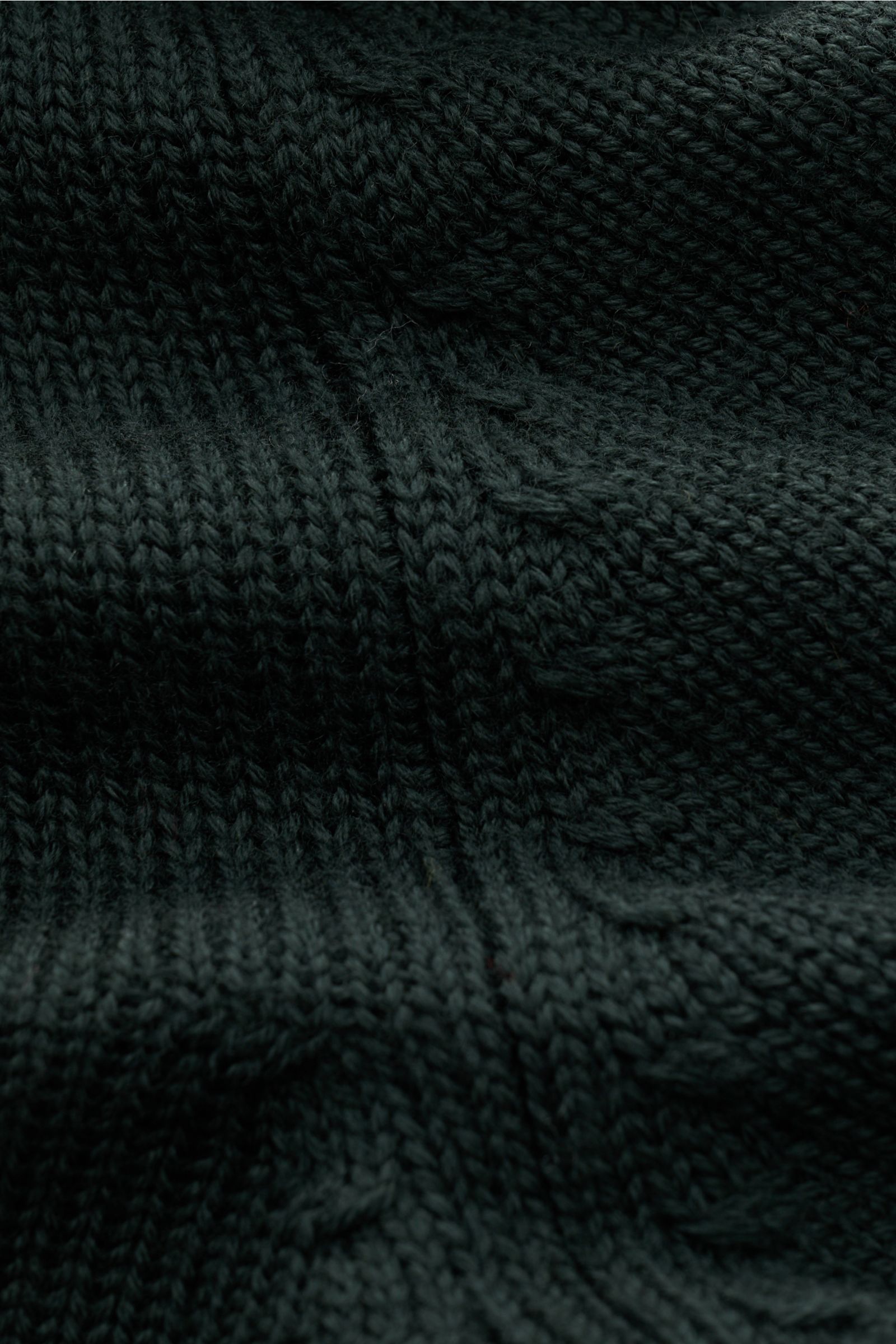 Nahaufnahme aus schräger Perspektive der dunkelgrünen B.F. Knitwear Merino Strickjacke mit mittelgrobem Strickbild aus reiner Merinowolle, weichem Griff, Stehkragen, Rundhalsausschnitt, Slim Fit, Zwei-Wege-Reißverschluss und komfortablen Rippbündchen.