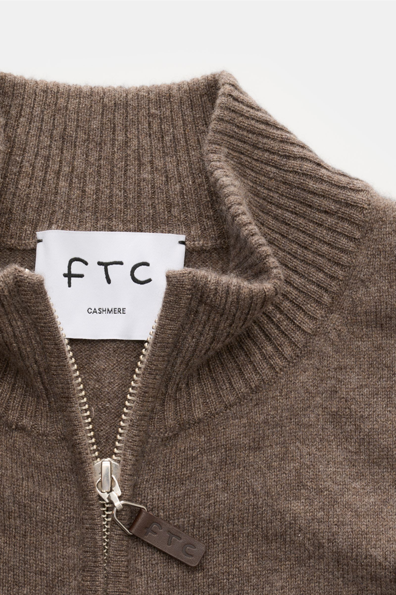 Nahaufnahme der FTC Cashmere Strickjacke graubraun aus Fair-Trade-Cashmere mit geripptem Stehkragen, verdecktem Zwei-Wege-Reißverschluss und Leder-Zipper-Detail, fotografiert von oben.