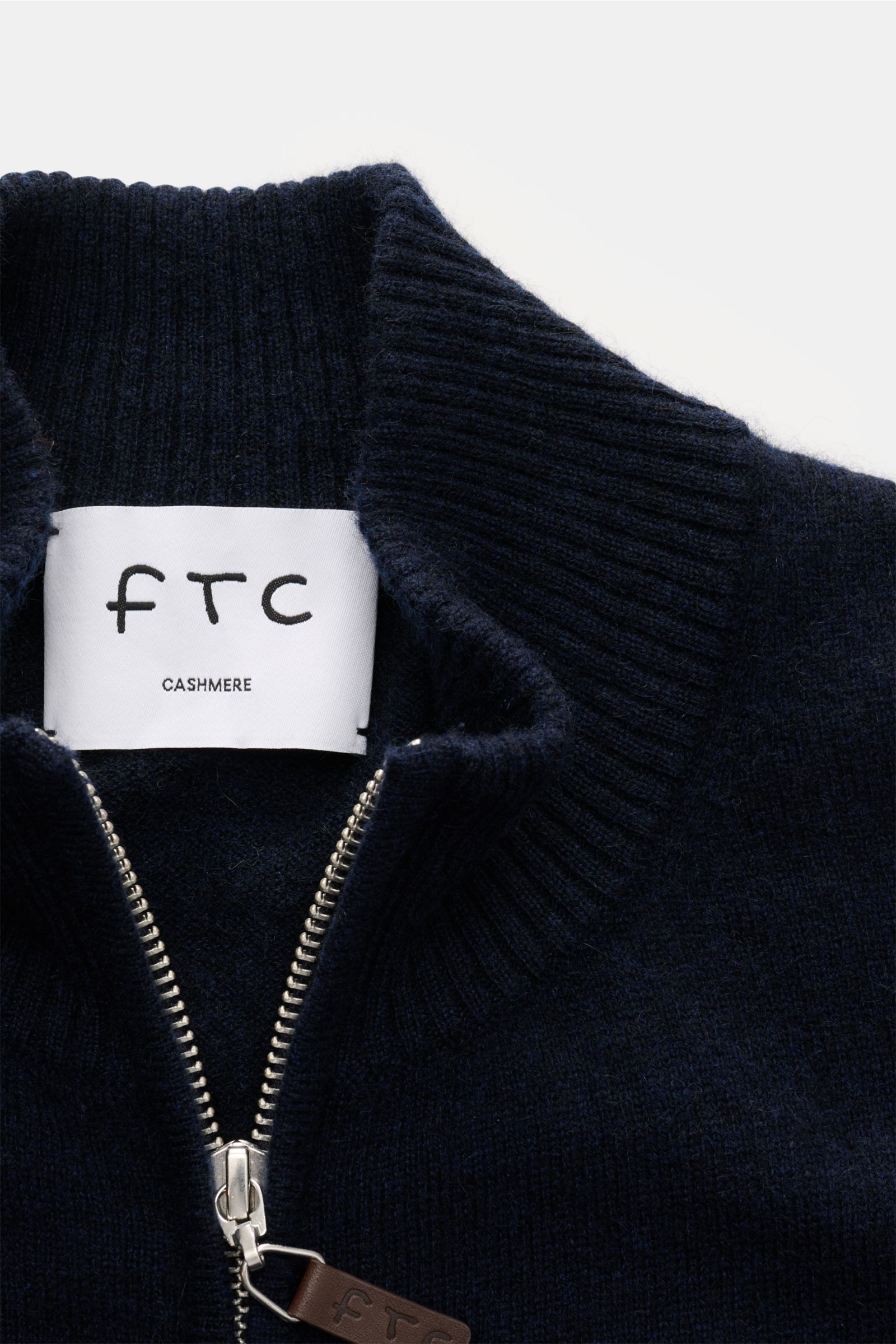 Nahaufnahme der FTC Cashmere Strickjacke navy von oben, zeigt gerippten Stehkragen, verdeckten Zwei-Wege-Reißverschluss mit Leder-Logo, fein gestrickt, Fair-Trade-Cashmere, sehr weich, Slim Fit.