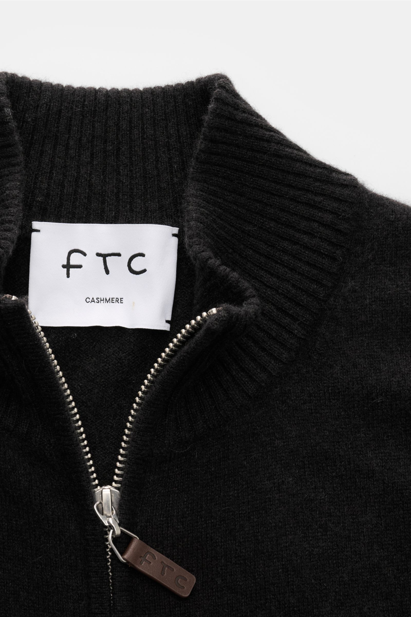 Nahaufnahme der FTC Cashmere Strickjacke dunkelbraun von oben, zeigt gerippten Stehkragen, verdeckten Zwei-Wege-Reißverschluss mit Leder-Logo und feines Strickbild. Fair-Trade-Cashmere, OEKO-TEX® Standard 100, Slim Fit, weicher Griff, flexible Rippbündche
