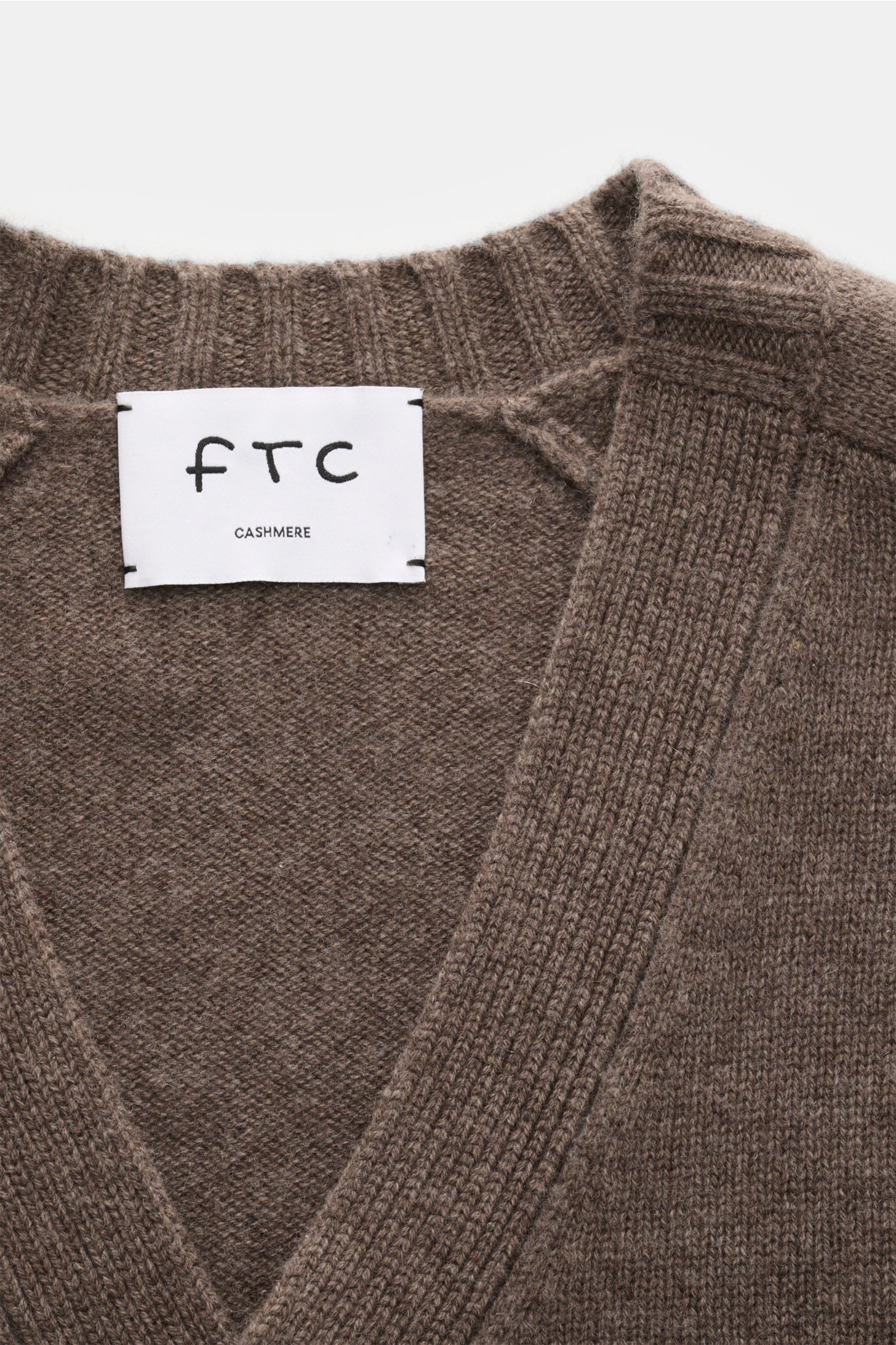 Nahaufnahme des FTC Cashmere Cardigan graubraun von oben fotografiert, V-Ausschnitt, weicher reiner Fair-Trade-Cashmere, Slim Fit, halbraglan-Ärmel, vier Knöpfe, Leistentaschen, Rippbündchen.