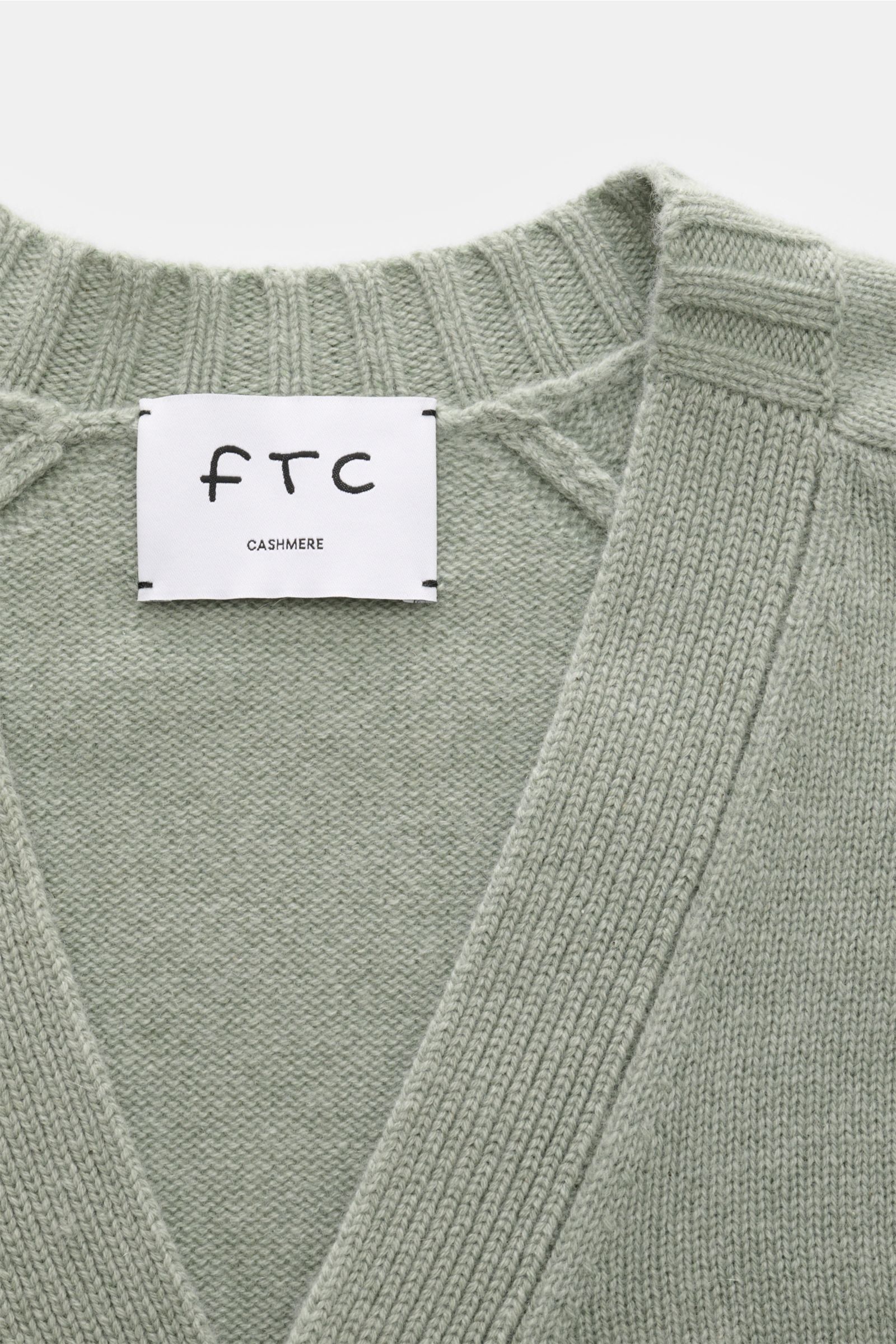 FTC Cashmere Cardigan graugrün in Nahaufnahme von oben, mittelfeines Strickbild, V-Ausschnitt, Halbraglan-Ärmel, weicher Fair-Trade-Cashmere, Label sichtbar.