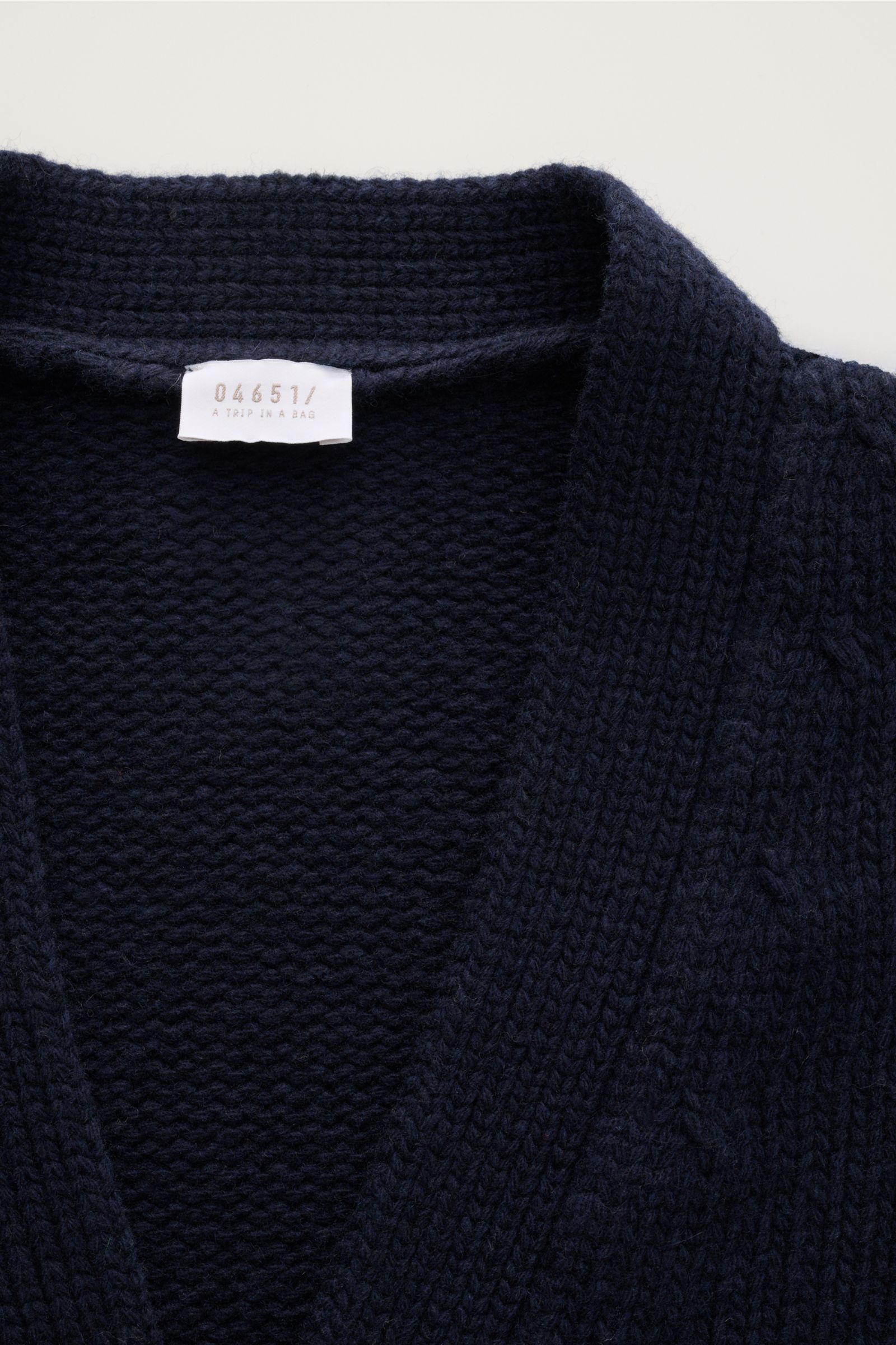 Nahaufnahme des dunkelblauen 04651/ A trip in a bag Cardigan 'Bold' navy aus reiner Lammwolle, grobes Strickbild, weicher Griff, Oversized Fit, mit Label innen am Kragen, fotografiert von oben.