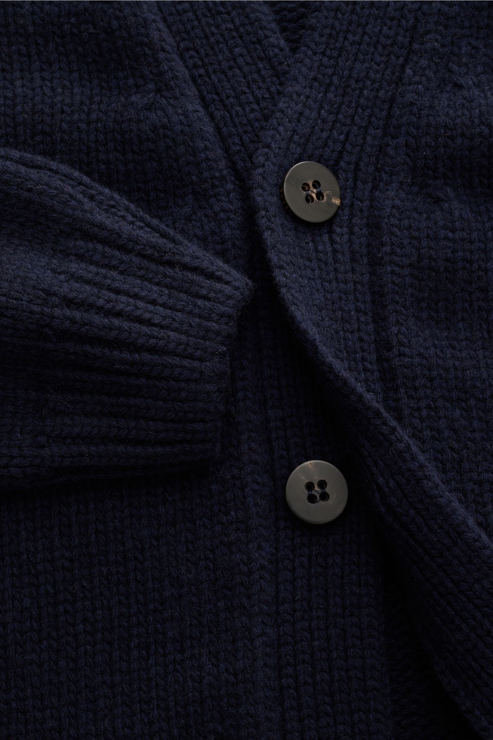 Nahaufnahme des grob gestrickten 04651/ A trip in a bag Cardigan 'Bold' navy aus reiner Wolle mit Oversized Fit, Vier-Knopf-Leiste und aufgesetzten Taschen, weich und markant, von oben fotografiert.