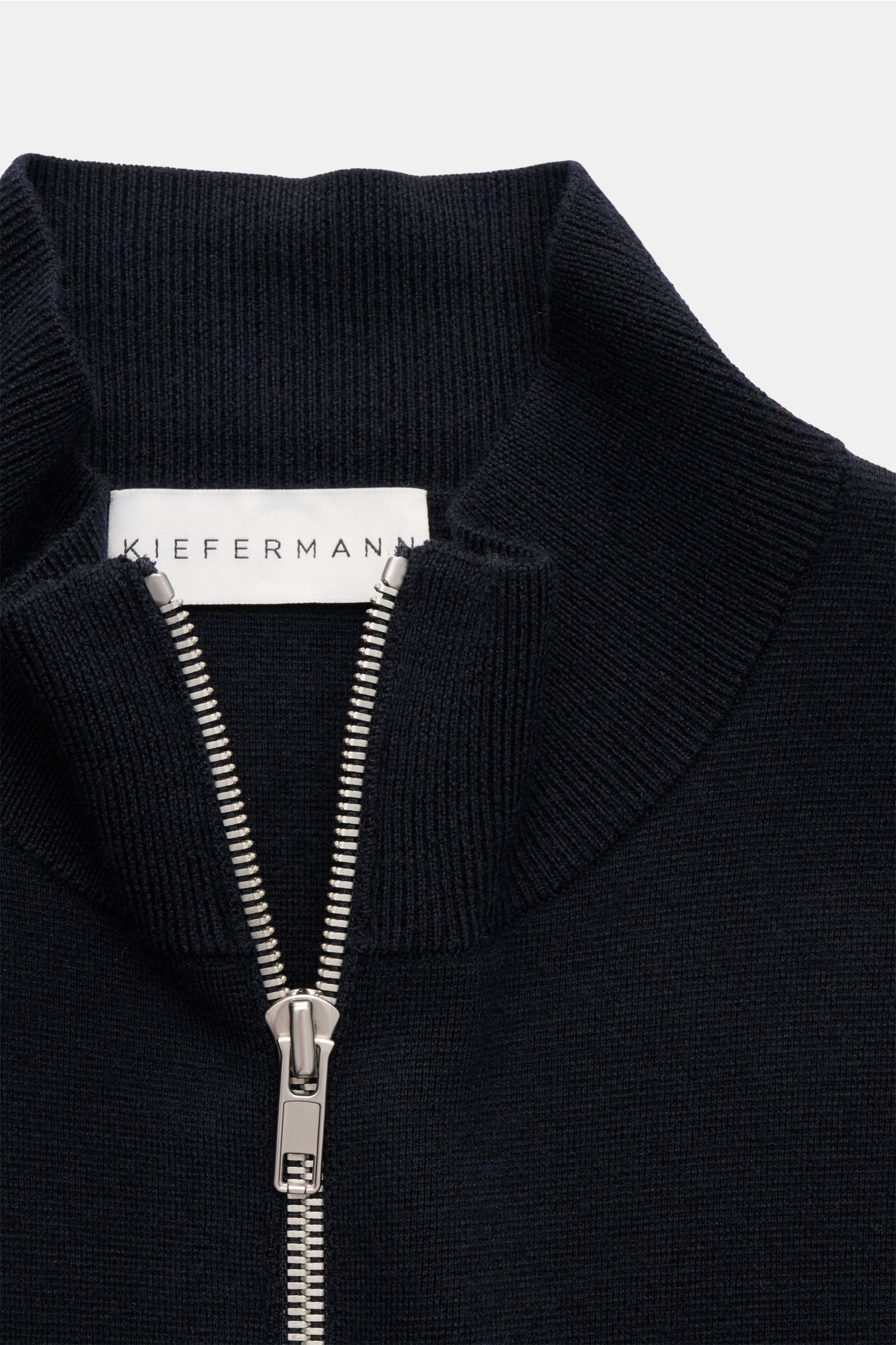 Nahaufnahme der Kiefermann Merino Strickjacke 'Dimitri' dark navy aus reiner Merinowolle mit Reißverschluss, Stehkragen, Slim Fit und flexiblem Rippbündchen, feinem Strickbild, weichem Griff, fotografiert von oben.