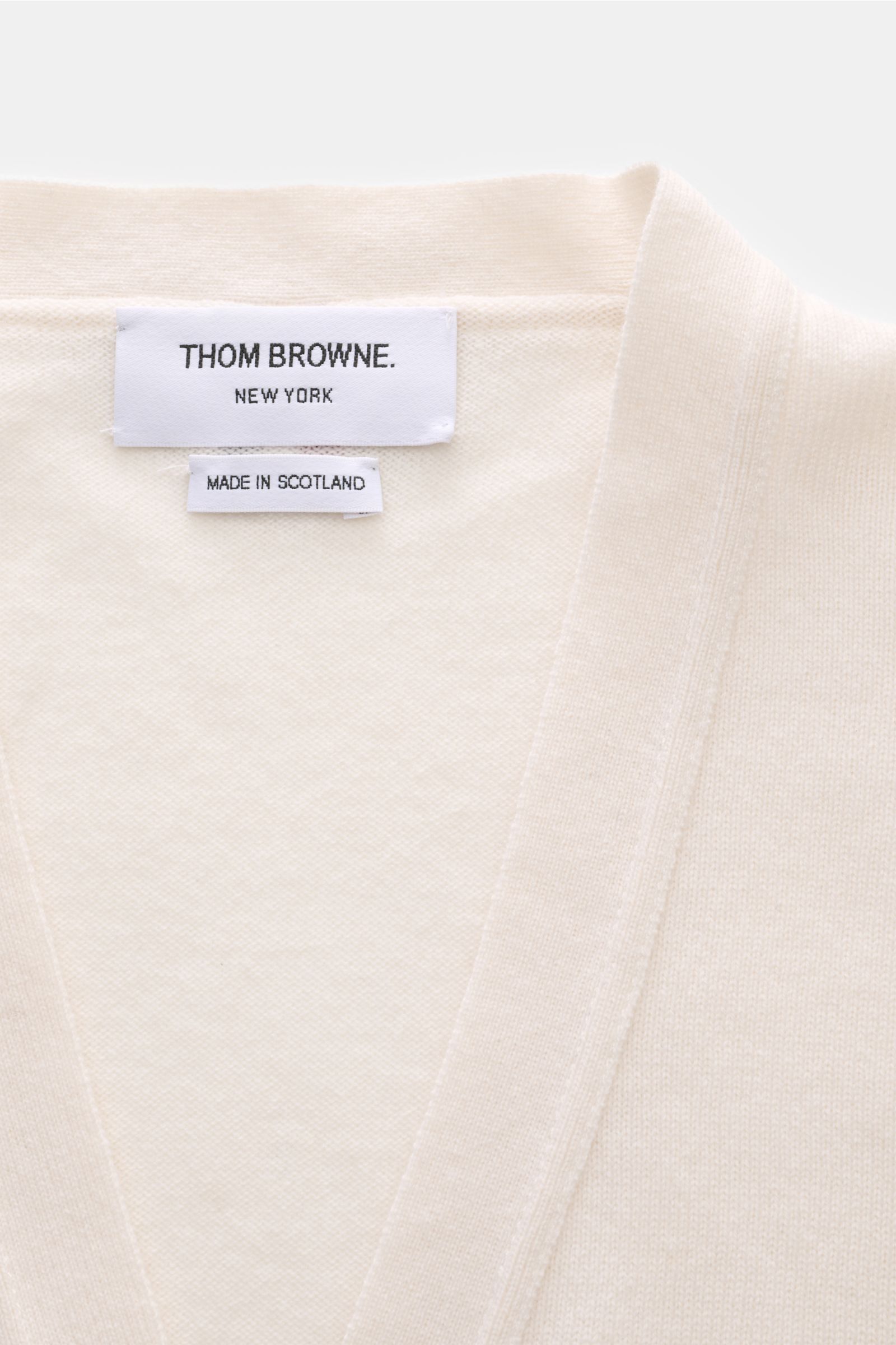 Close-up front top view of Thom Browne Cashmere Cardigan offwhite showing pure cashmere fabric, soft texture, fine knit, and neckline with brand label.

Vielseitiger Style-Favorit: Der Cashmere Cardigan von THOM BROWNE kombiniert luxuriöse Materialien 