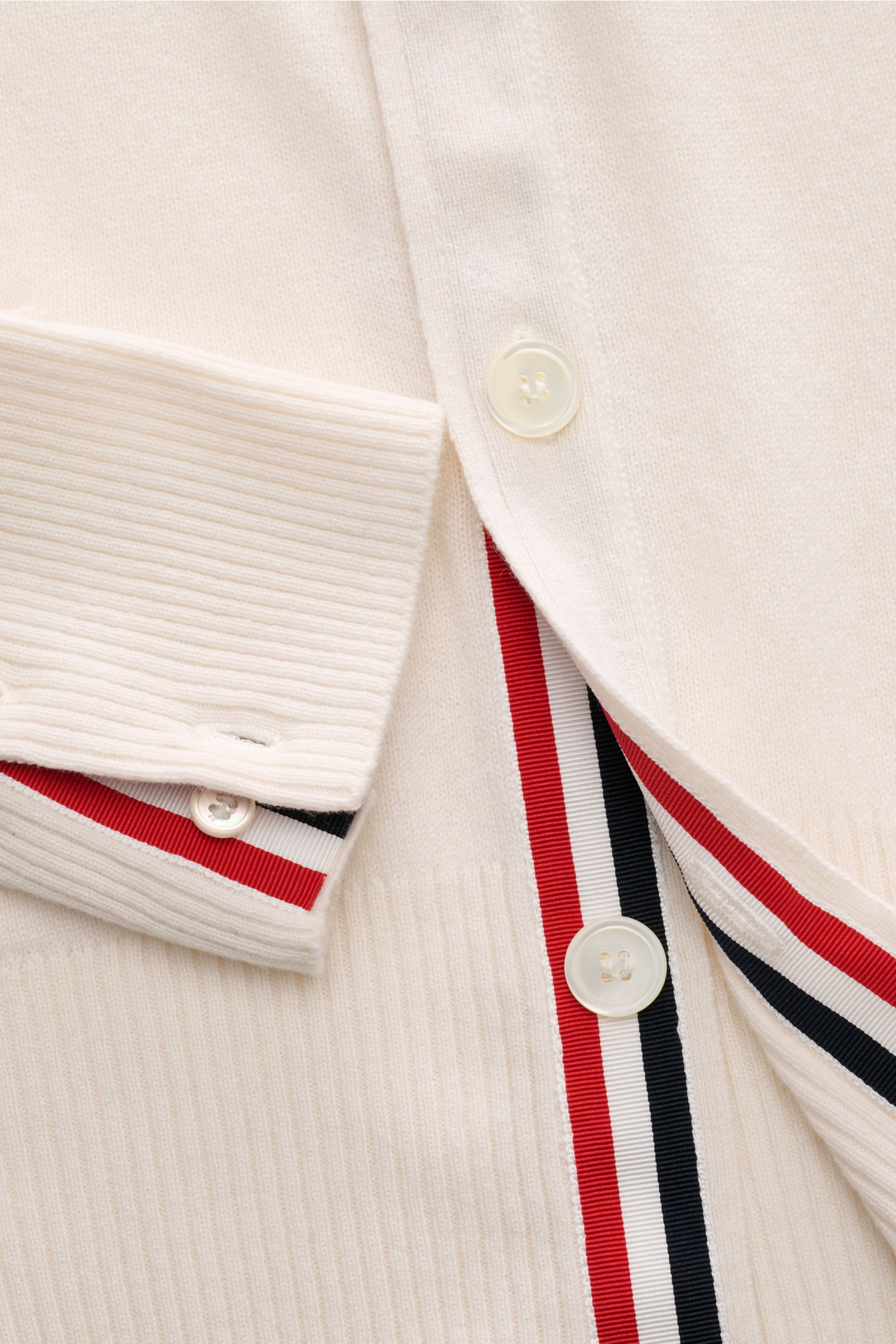 Close-up front view of Thom Browne Cashmere Cardigan offwhite showing buttoned cuff, ribbed knit, and red-white-black striped trim with buttons.

The provided content in English for reference:  
Versatile style favorite: The Cashmere Cardigan by THOM BROW