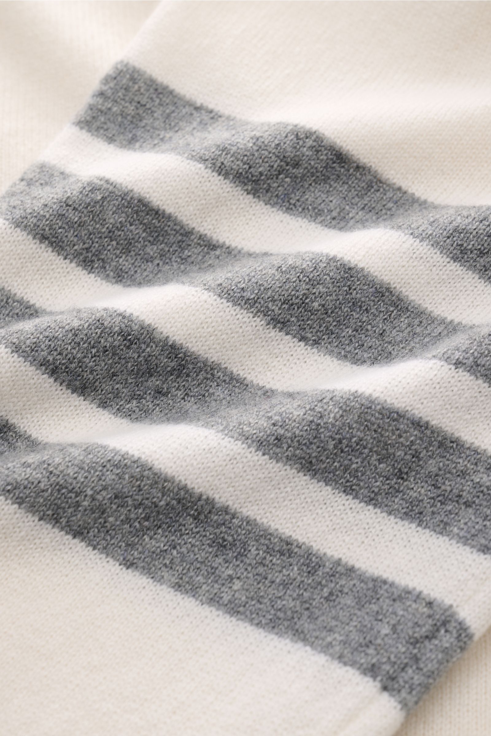 Close-up front view of the Thom Browne Cashmere Cardigan offwhite showing soft, fine knit fabric with offwhite and grey stripes, highlighting its pure cashmere, soft touch, regular fit, button placket, patch pockets, wide rib cuffs, and side slits with bu