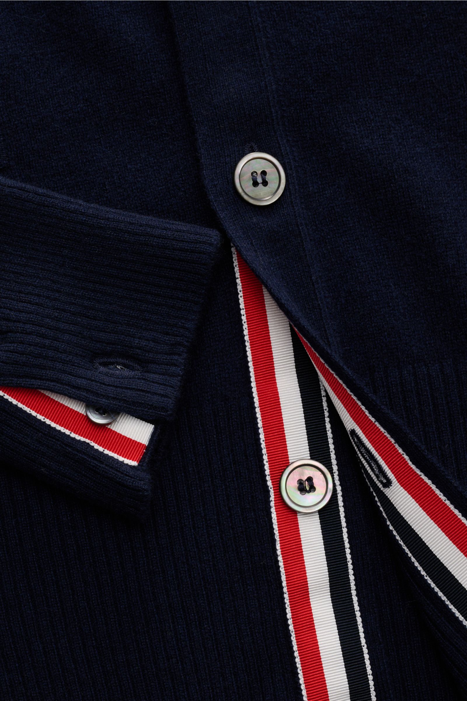 Close-up front view of Thom Browne Cashmere Cardigan navy showing ribbed cuff, mother-of-pearl buttons, and red-white-blue striped trim with fine knit texture.
