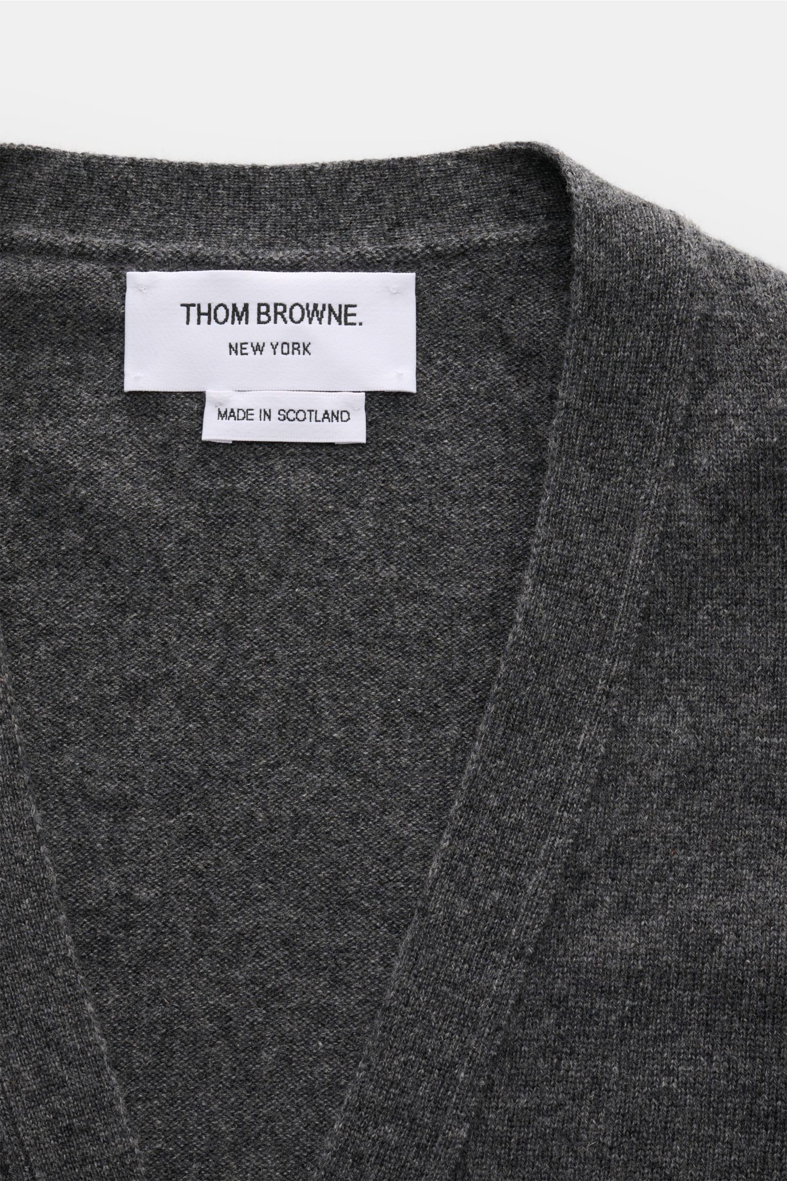 Close-up front view of Thom Browne Cashmere Cardigan dunkelgrau meliert showing soft, fine knit, ribbed collar, and brand label.  

Additional content:  
Vielseitiger Style-Favorit: Der Cashmere Cardigan von THOM BROWNE kombiniert luxuriöse Materialien