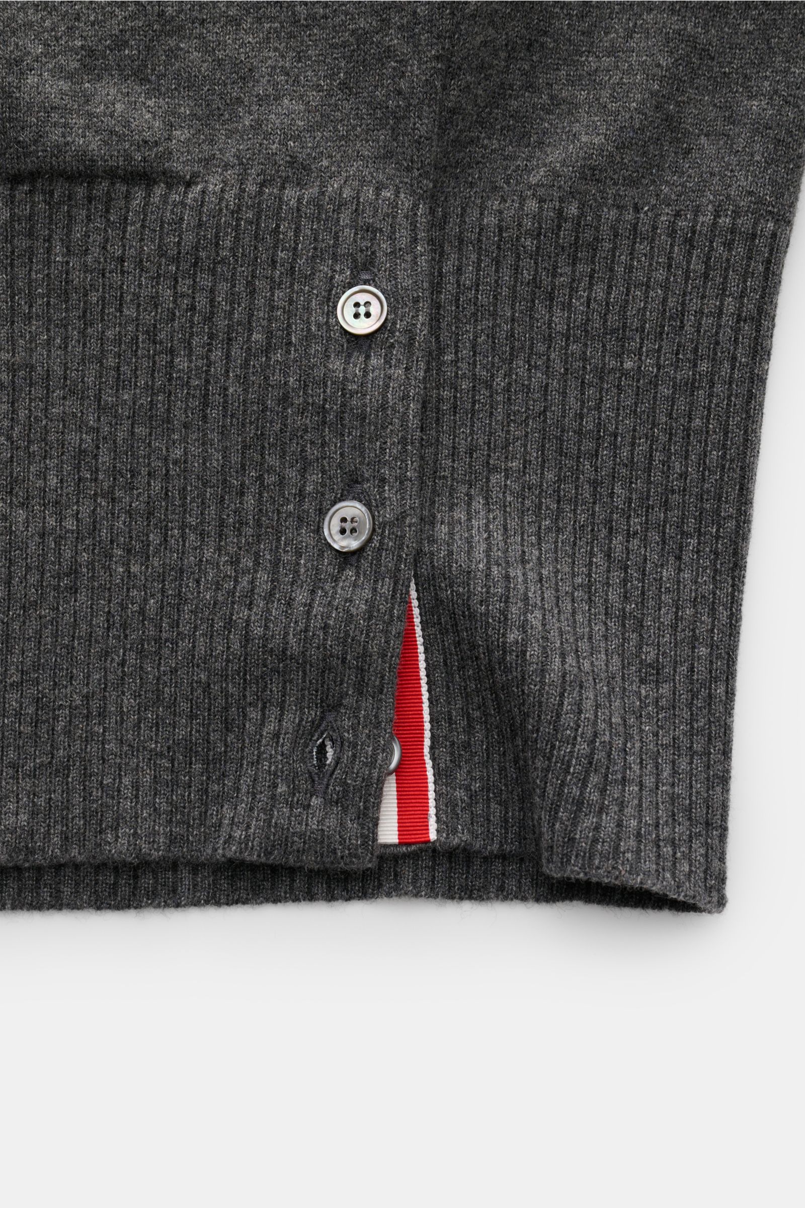 Close-up front view of Thom Browne Cashmere Cardigan dunkelgrau meliert showing ribbed knit, button placket, side slit with buttons, and red-white stripe detail.

Description: Vielseitiger Style-Favorit: Der Cashmere Cardigan von THOM BROWNE kombiniert lu