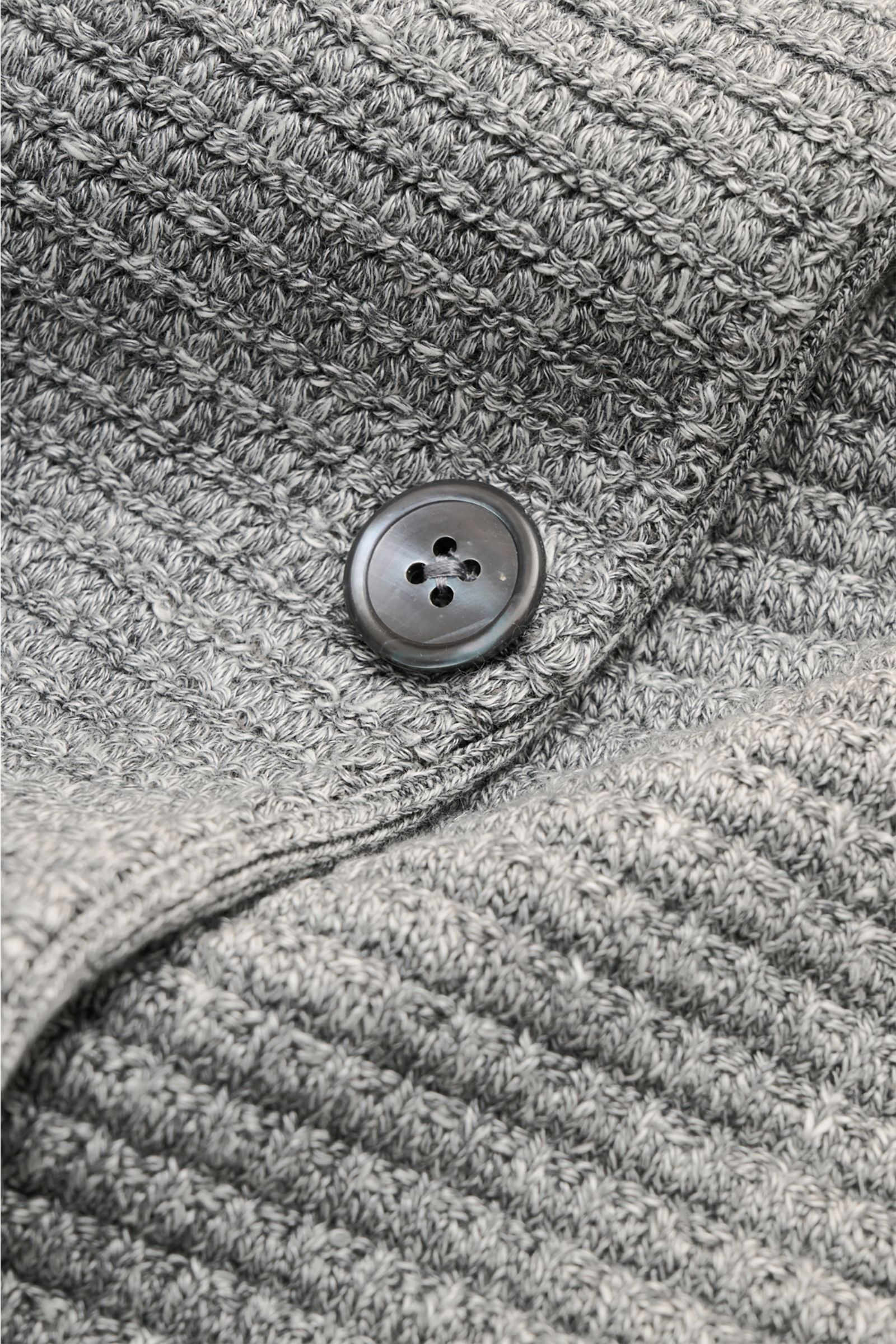 Nahaufnahme des Thom Browne Cardigan hellgrau meliert mit markantem Strickmuster, Knopf und Tricolore-Details aus Leinen, Baumwolle und Microfaser.