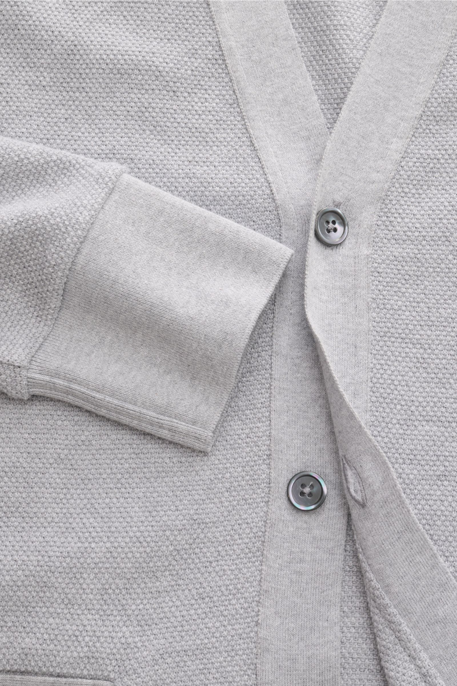 Close-up front view of the Thom Browne Cardigan light grey mottled, showing dark mother-of-pearl buttons, finely textured pure cotton knit fabric, V-neck, flexible sleeve cuff, and contrasting tricolour ribbed band details. 

This cotton cardigan by TH