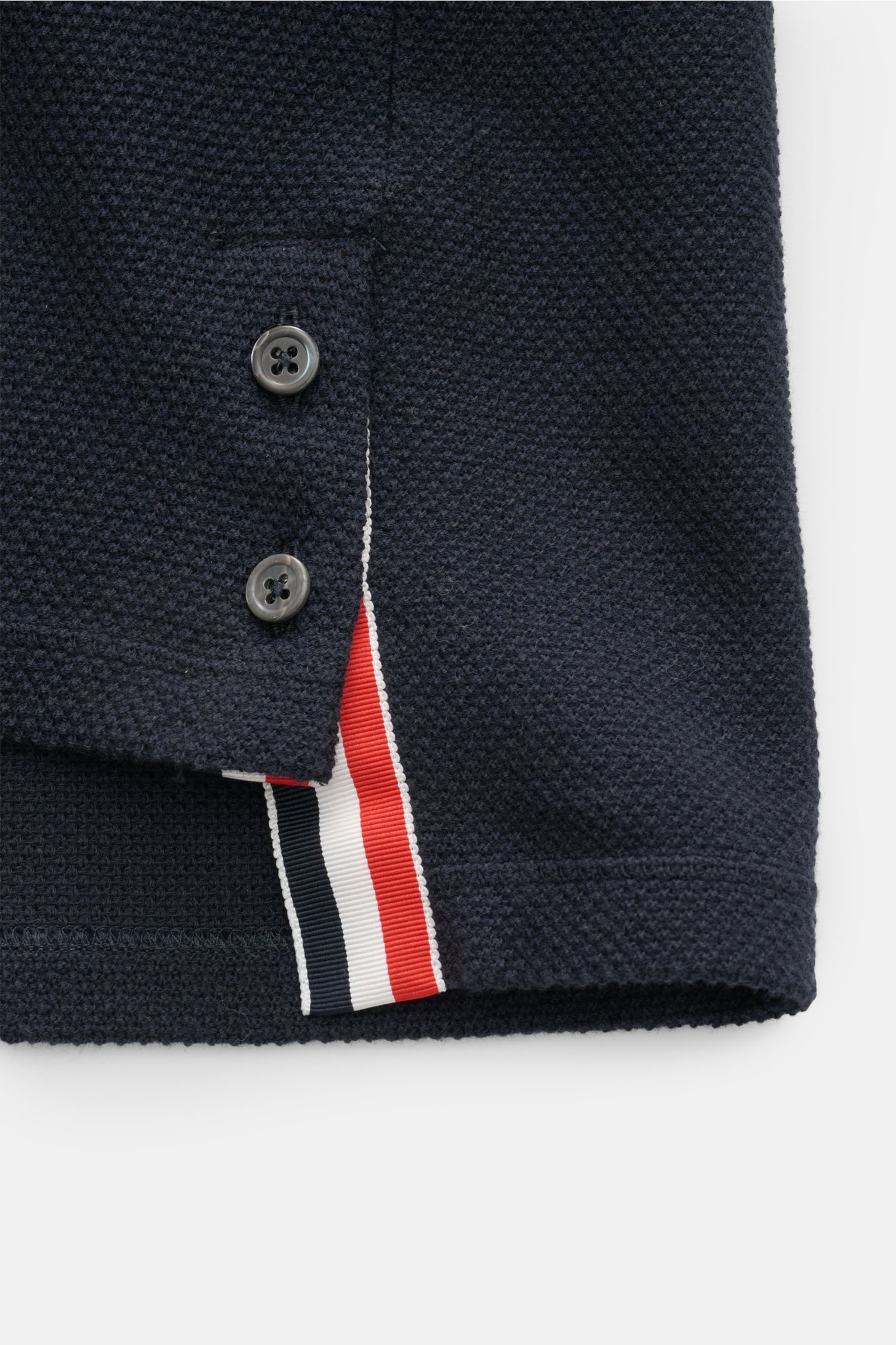 Close-up side view of Thom Browne Cardigan navy showing dark mother-of-pearl buttons, tricolour ribbed band accents, and textured knit fabric. 

This cotton cardigan by THOM BROWNE combines a campus aesthetic with modern accents: distinctive contrastin