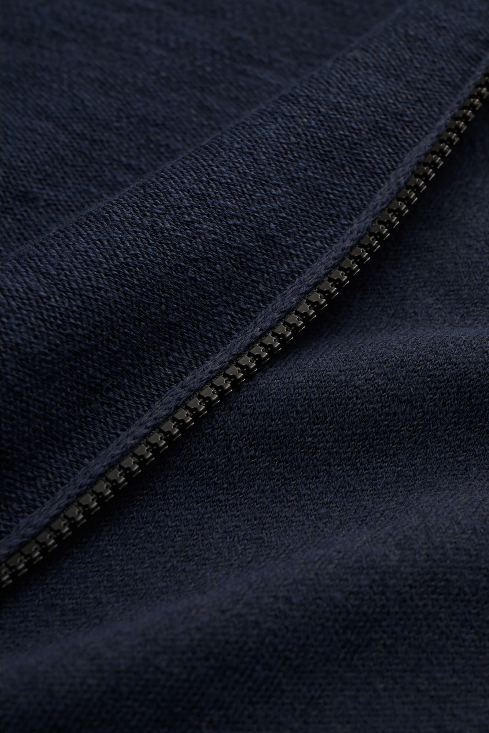 Nahaufnahme aus schräger Perspektive einer Stone Island Sweatjacke navy mit Reißverschluss, linksgestrickter Baumwoll-Microfaser-Mischung, Kapuze und Rippstrickbündchen.