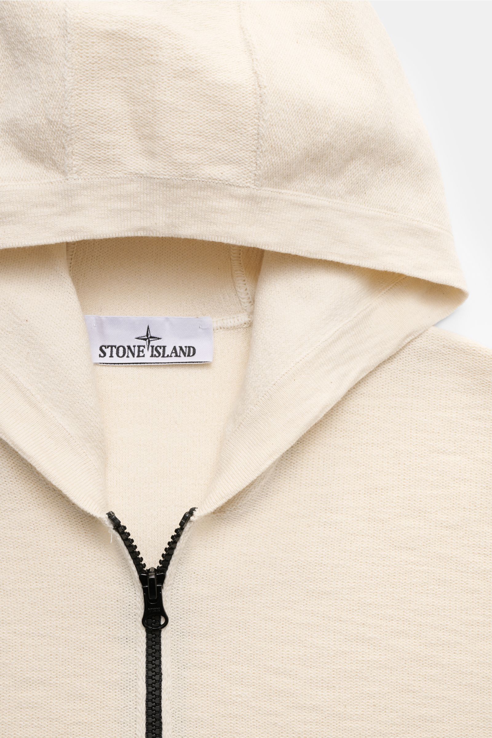 Close-up front view of Stone Island Sweatjacke creme hoodie with black zipper, showing creamy links knit texture and Stone Island label inside.

Description: Strick mit Twist: Die sportive Jacke mit Kapuze im modernen Linksstrick von STONE ISLAND wird 