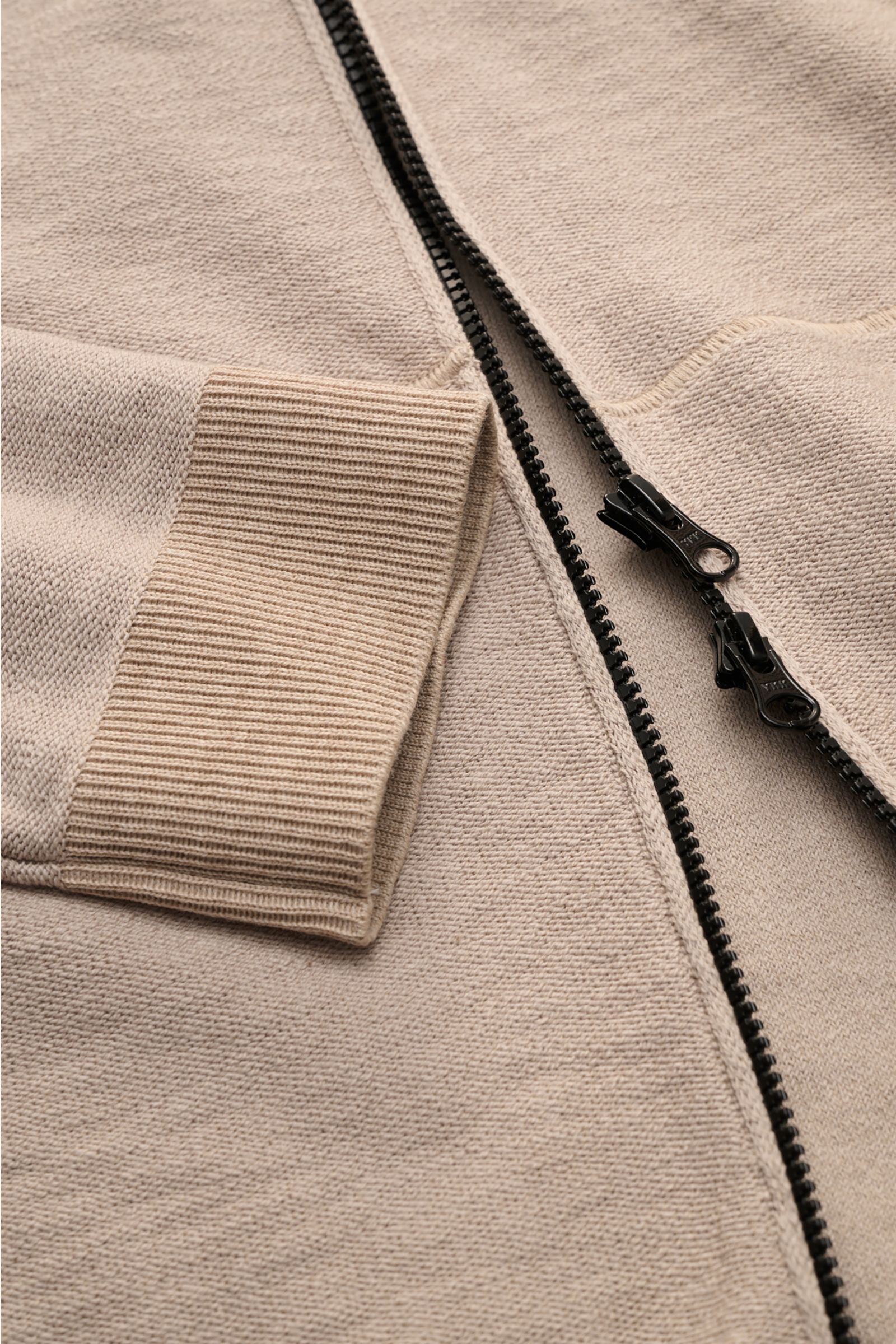 Nahaufnahme der Stone Island Sweatjacke beige im Linksstrick, Fokus auf Reißverschluss, Rippstrickbündchen und geteilte Kängurutasche.