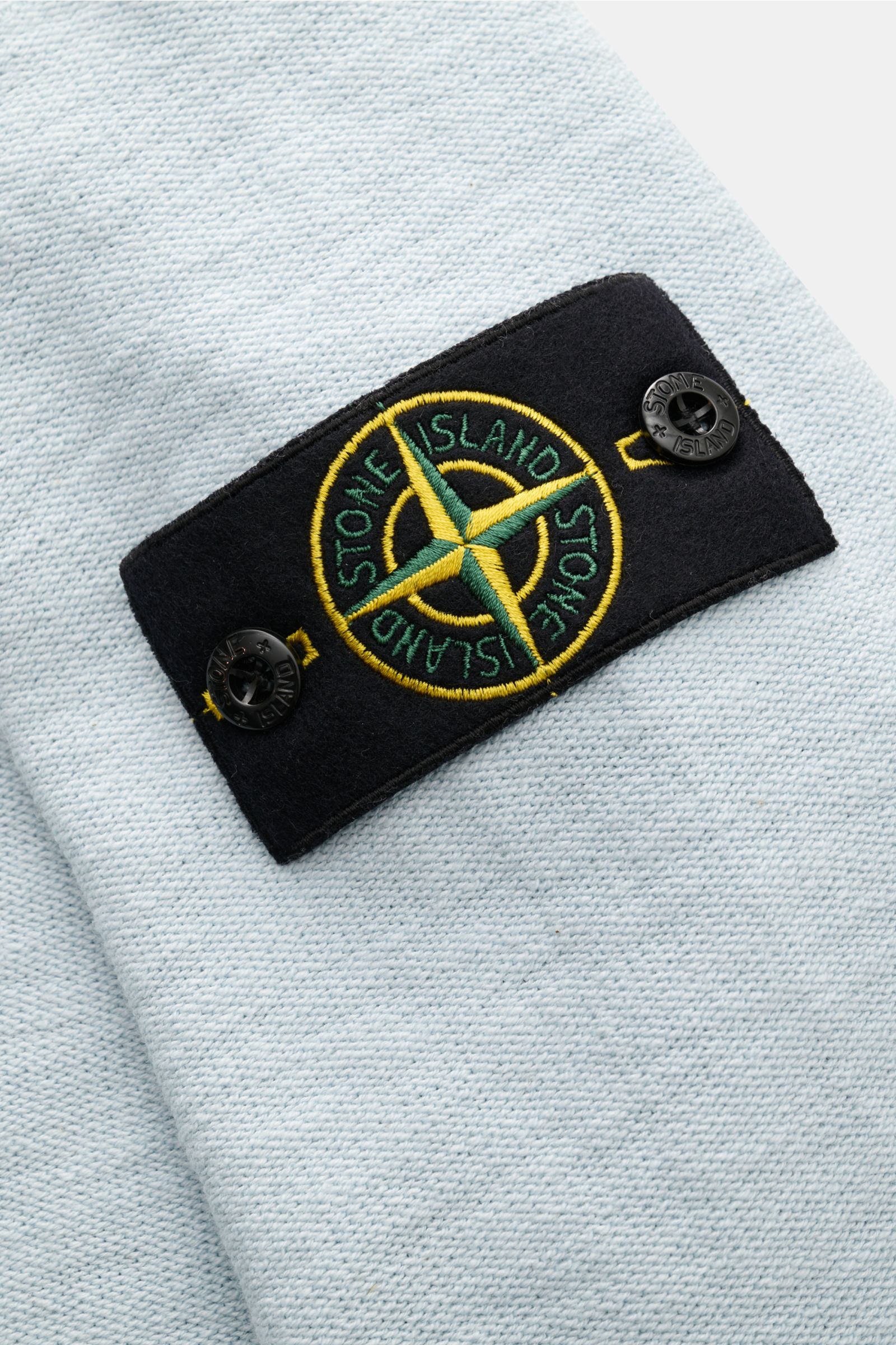 Close-up of the Stone Island Sweatjacke pastellblau showing the brand’s compass badge on the sleeve, photographed from the side. Strick mit Twist: Die sportive Jacke mit Kapuze im modernen Linksstrick von STONE ISLAND wird zum idealen Freizeitbegleiter un