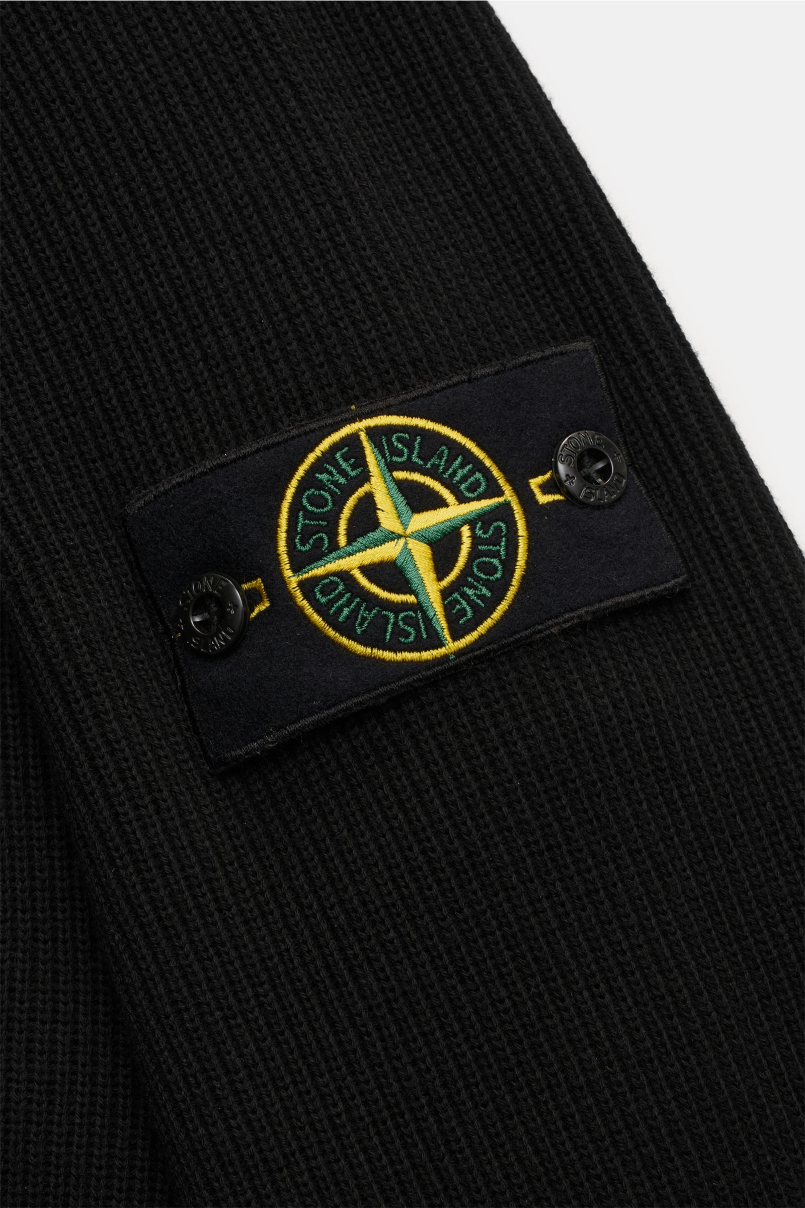 Close-up side view of Stone Island Strickjacke 'Rib' schwarz showing black ribbed knit cotton fabric with a soft texture and the signature compass badge on the upper arm.

Zeitloses Layering-Piece: Die Strickjacke von STONE ISLAND wird mit ihrem Rippst