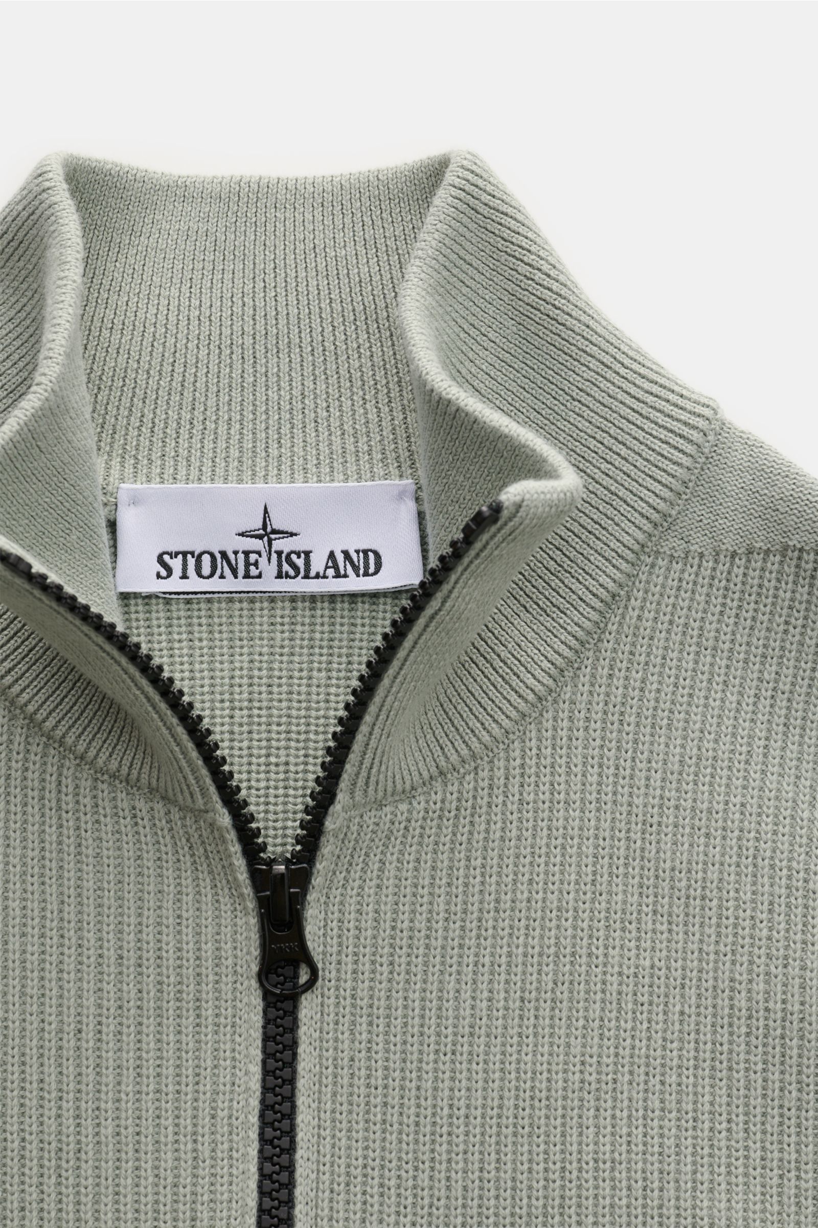 Stone Island Strickjacke 'Rib' salbei shown from close-up front top view, featuring ribbed knit design, soft pure cotton, two-way zipper, standing collar, and Stone Island label inside collar. Zeitloses Layering-Piece: Die Strickjacke von STONE ISLAND wir
