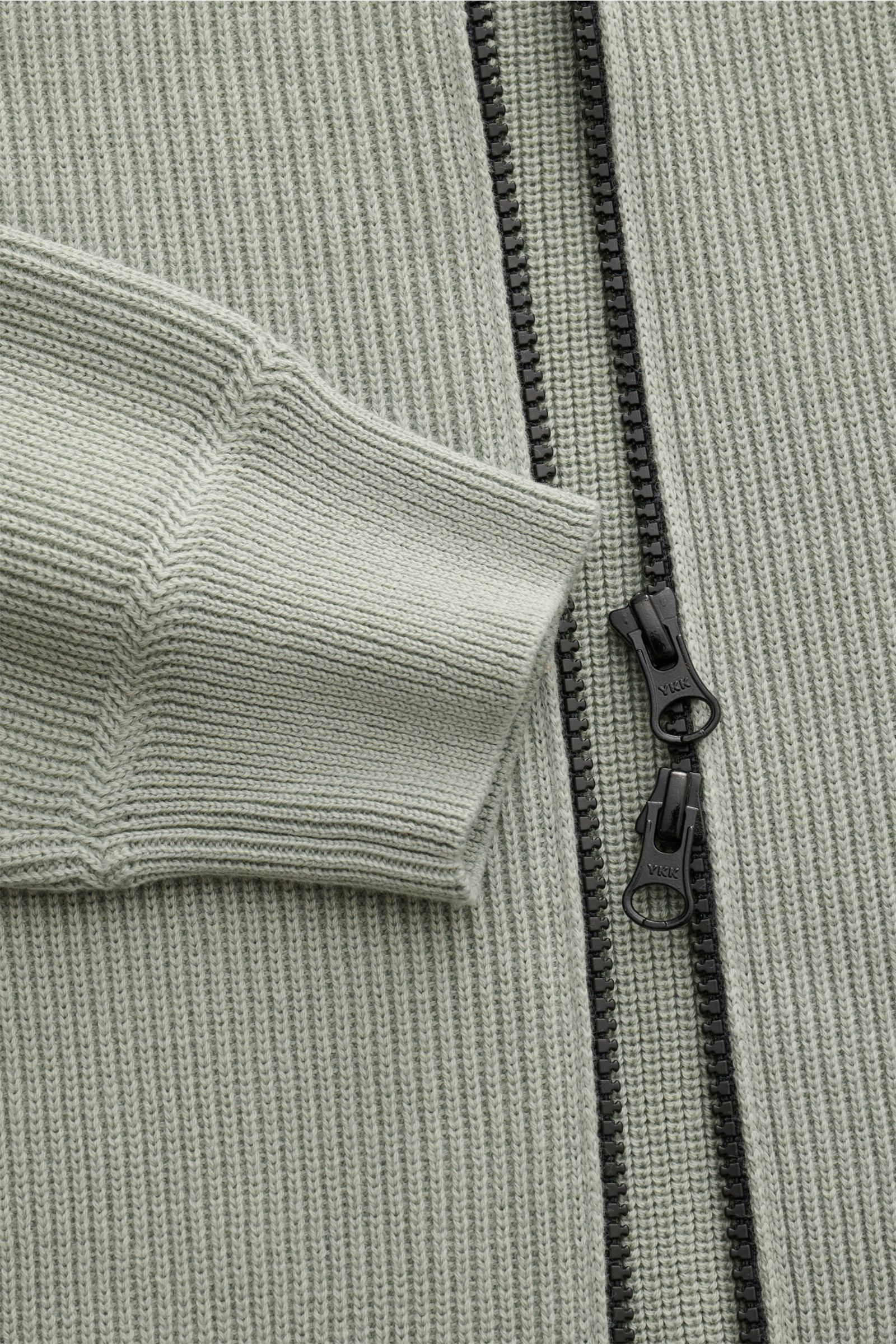 Close-up top view of Stone Island Strickjacke 'Rib' salbei showing ribbed knit texture, two-way black zipper, and cuff detail.  
Zeitloses Layering-Piece: Die Strickjacke von STONE ISLAND wird mit ihrem Rippstrick-Design aus reiner Baumwolle zum vielse