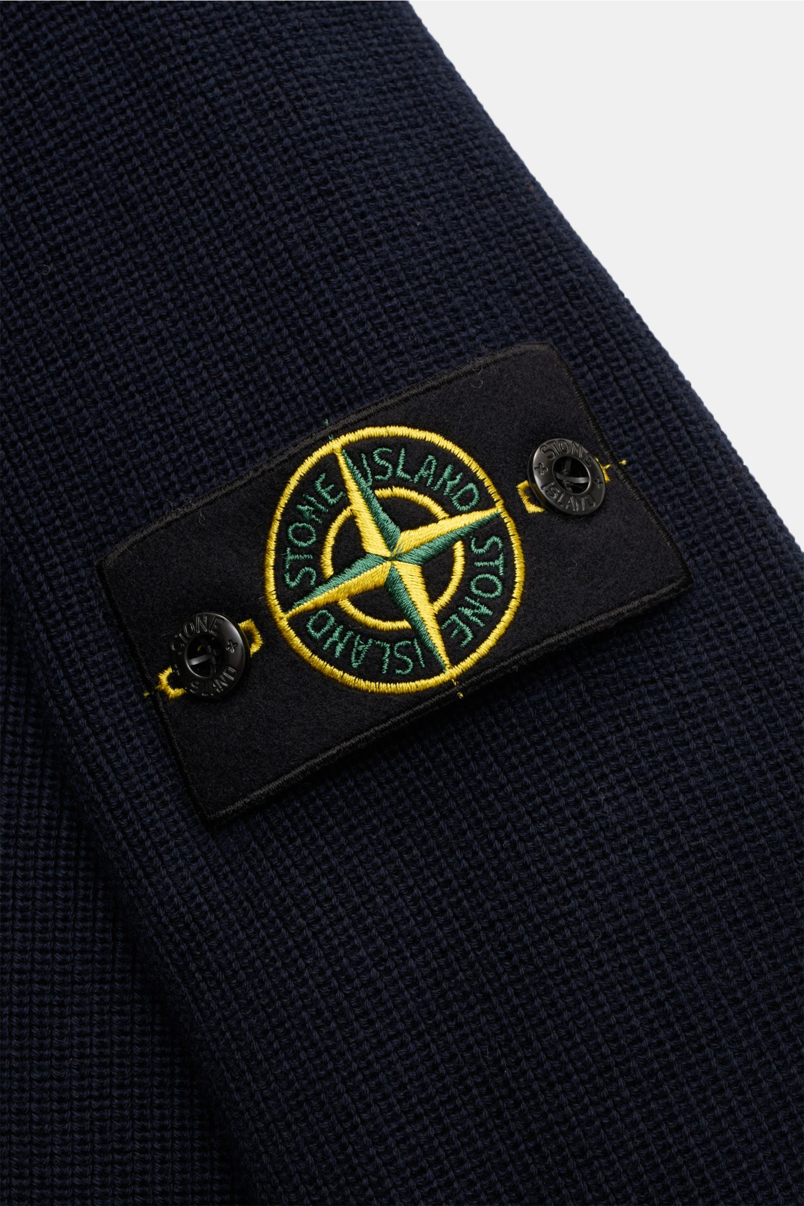 Nahaufnahme des Stone Island Cardigan navy aus reiner Baumwolle mit feinem Rippstrick-Design und Kompass-Badge am Ärmel, schräg von oben fotografiert.