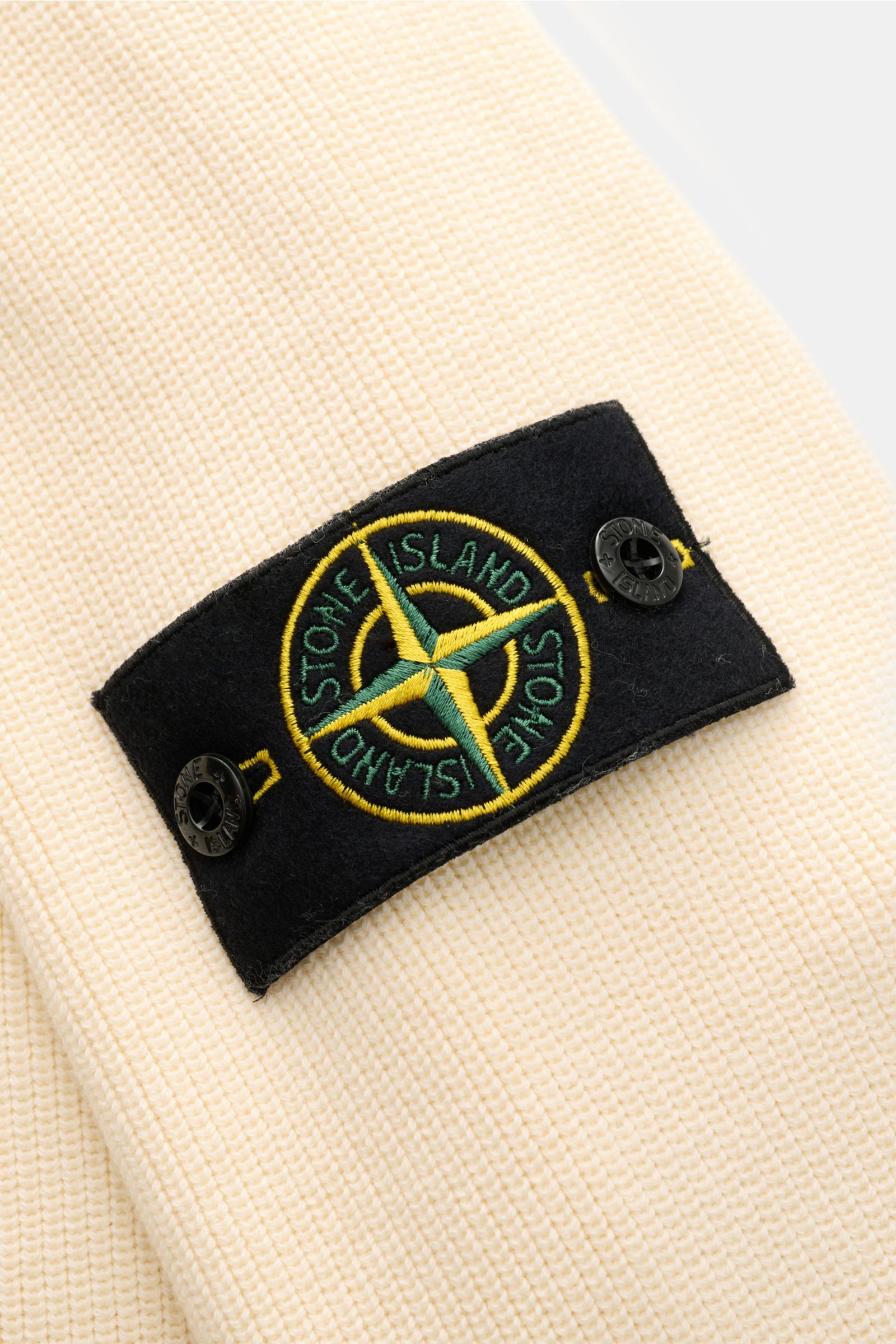 Nahaufnahme des Kompass-Badges auf dem Oberarm des Stone Island Cardigan creme aus feinem Rippstrick, reine Baumwolle.