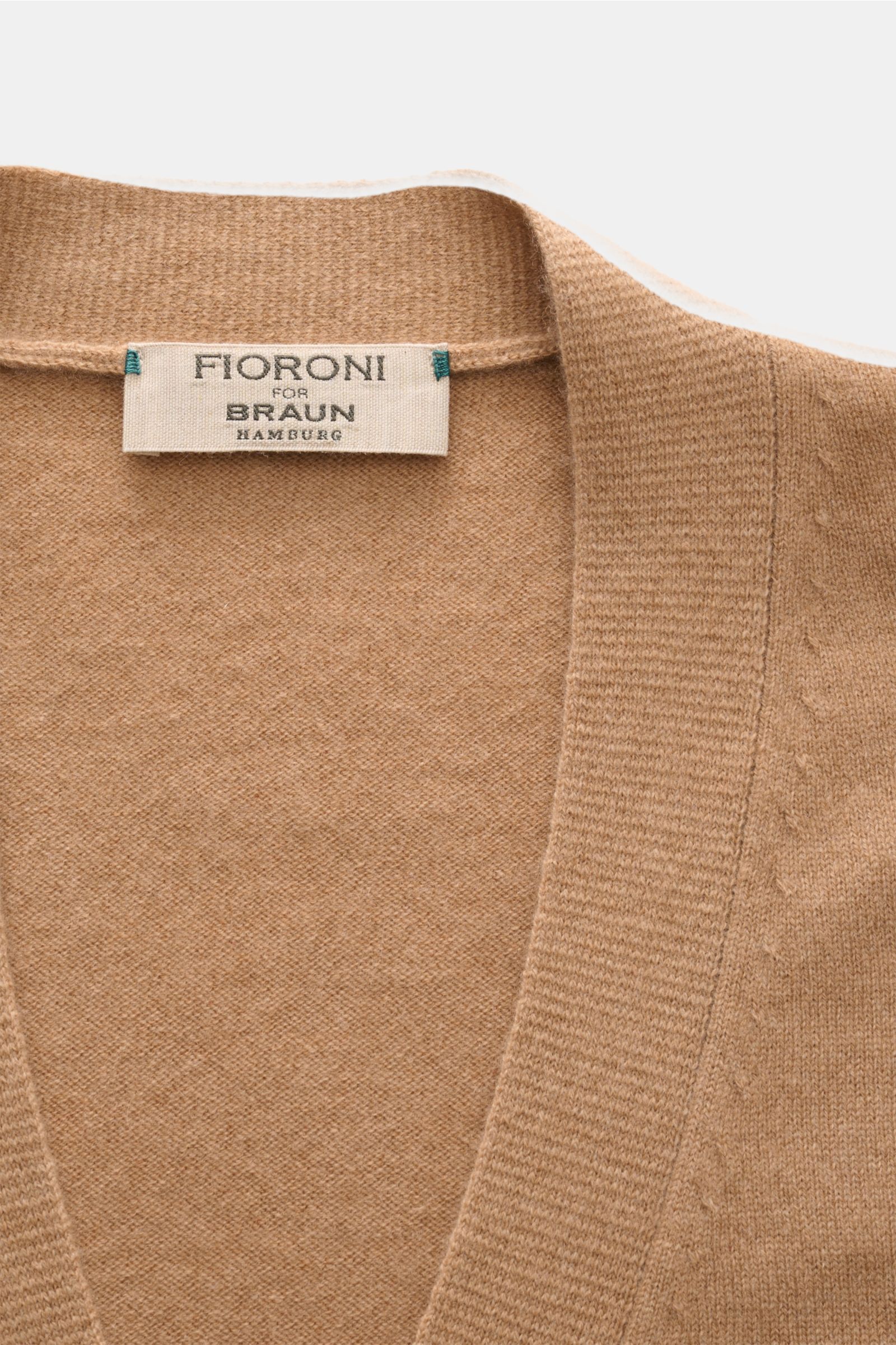 Close-up top view of Fioroni Cashmere cardigan light brown mottled showing fine knit texture and label with exquisite craftsmanship from Italy, made of pure baby cashmere with a slim fit, smooth button placket, and flexible ribbed bands.