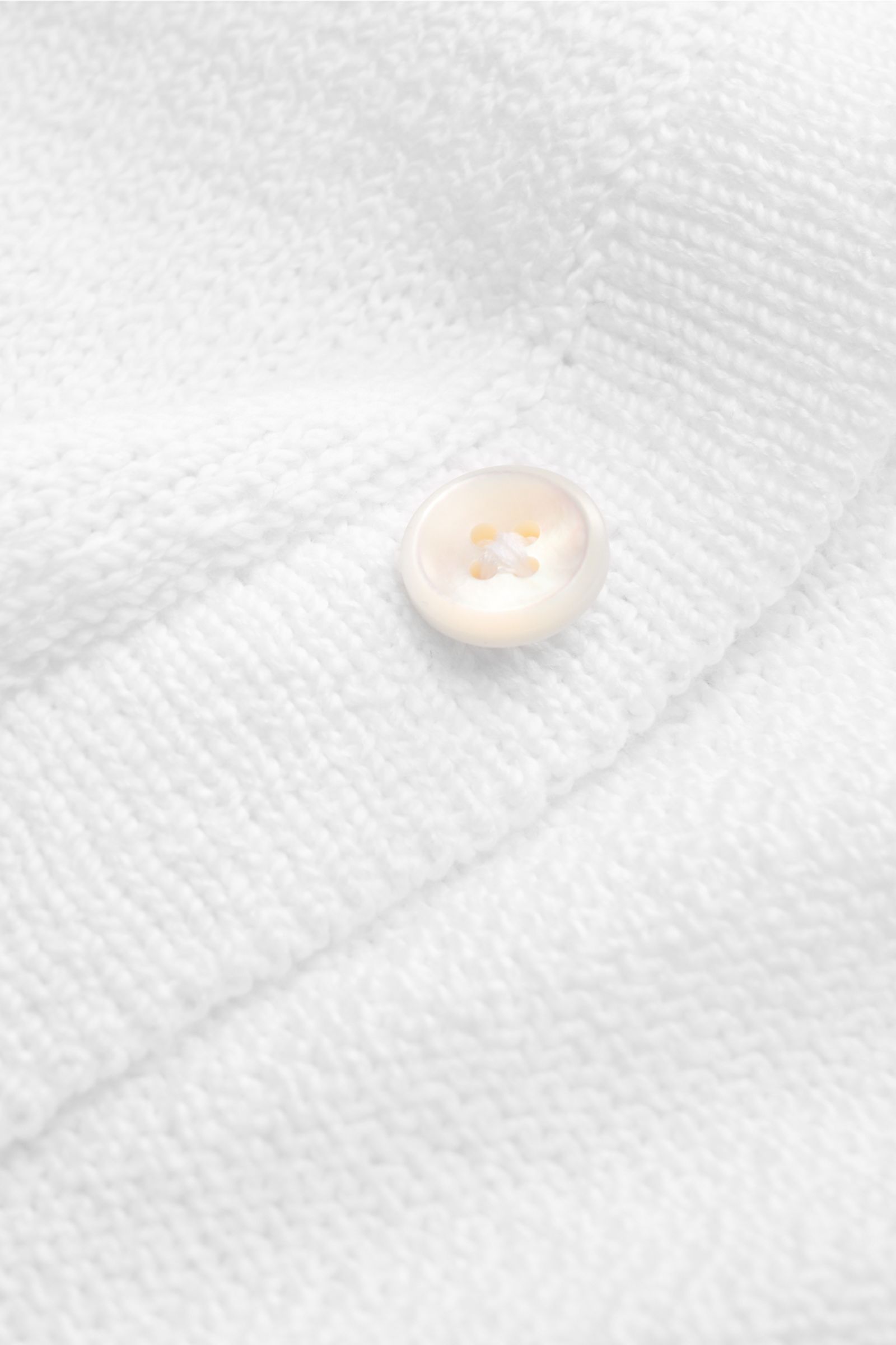 Nahaufnahme des weißen Fioroni Cardigan mit acht Knöpfen, Umlegekragen, Slim Fit und feinem Strick aus reiner Baumwolle.