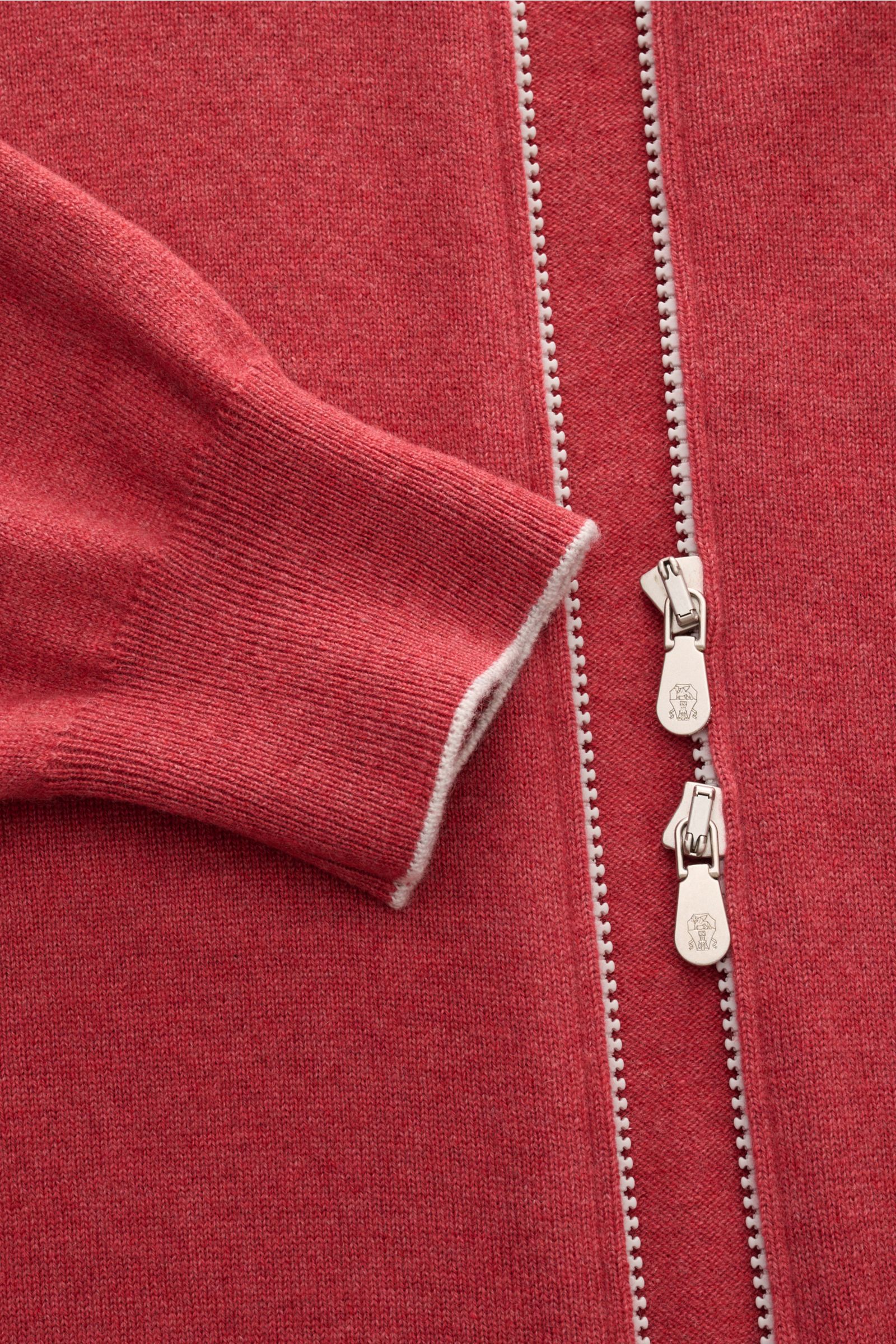 Close-up top-down view of the Brunello Cucinelli Cashmere Strickjacke hellrot showing soft light red cashmere fabric, fine knit, narrow white contrast edges on sleeve cuff, and a practical two-way silver zipper with branded pulls.

Luxus für die Freize