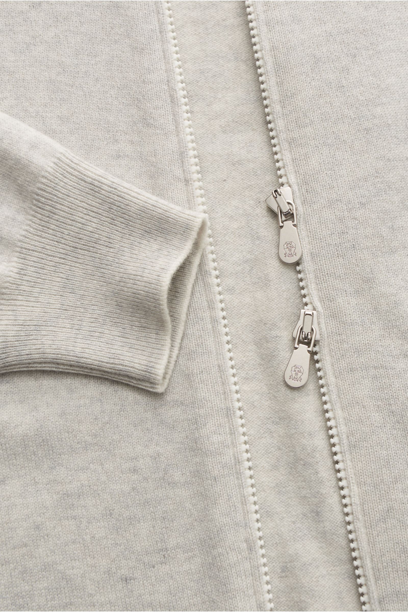 Close-up front view of Brunello Cucinelli Cashmere Strickjacke hellgrau meliert, showing soft light grey melange cashmere fabric, two-way zipper with logo pulls, and ribbed cuff with fine contrasting edges.

Luxus für die Freizeitgarderobe bietet BRUNE