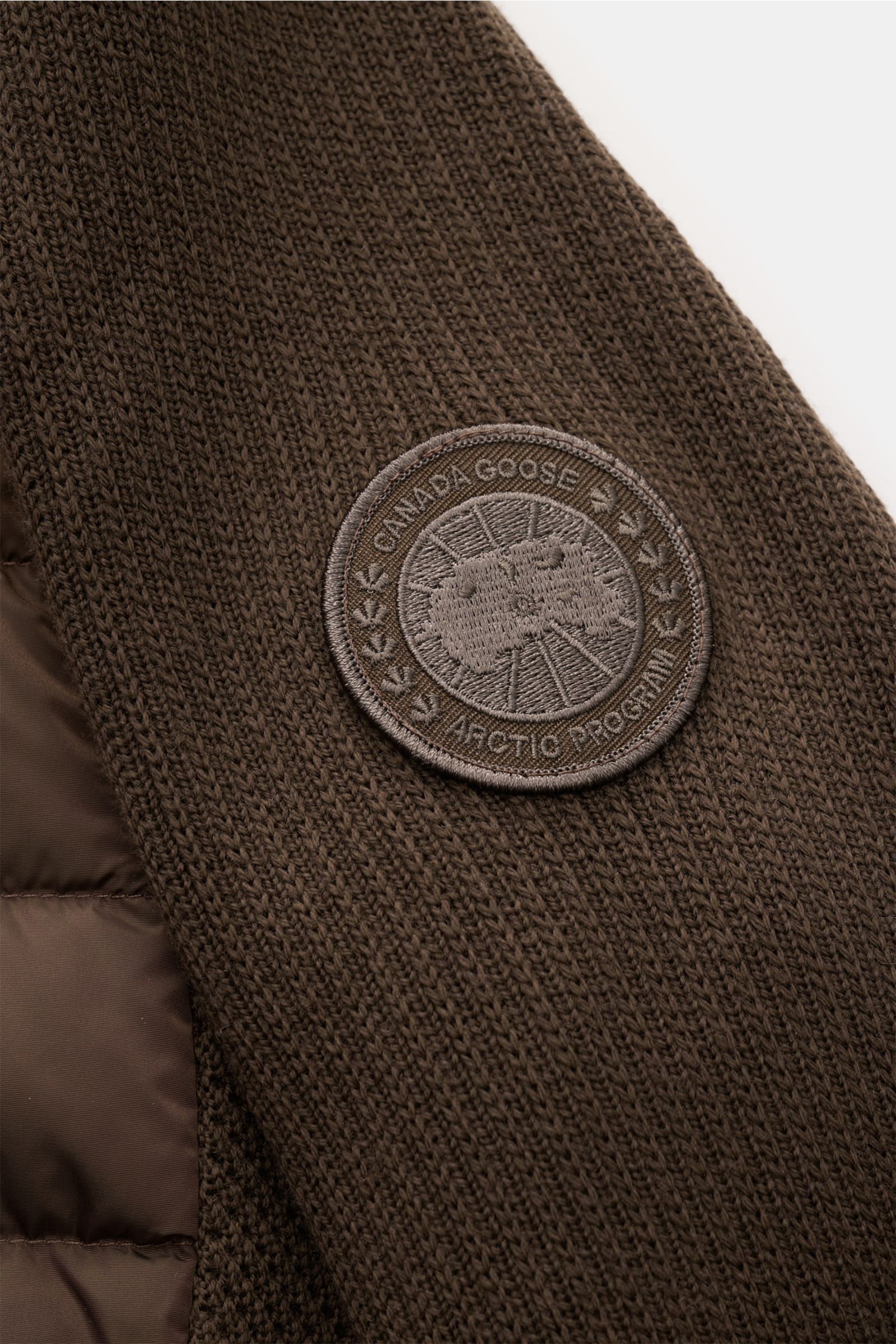 Canada Goose Cardigan 'Hybridge Knit' dark brown, close-up of sleeve's textured pure wool knit and woven label, photographed from above. 

Make a smooth transition into the new season with the cardigan 'Hybridge Knit' from the outdoor label CANADA GOOS