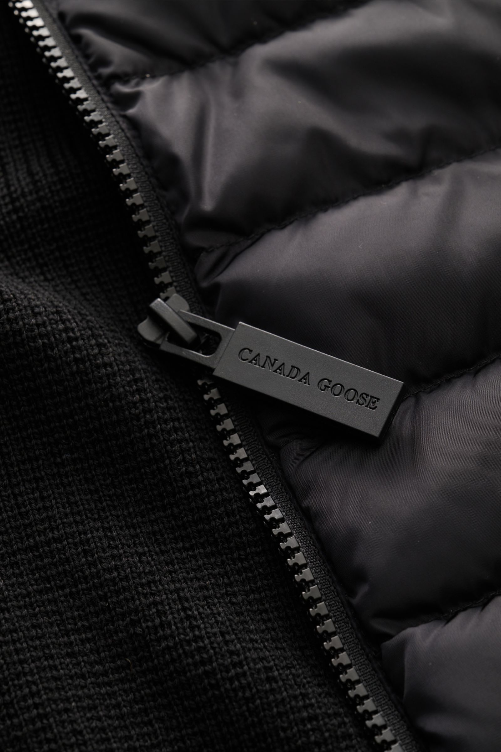 Nahaufnahme aus schräger Perspektive der Canada Goose Strickjacke 'Hybridge Knit' schwarz mit Daunen-Front, Wollstrick und Reißverschluss.