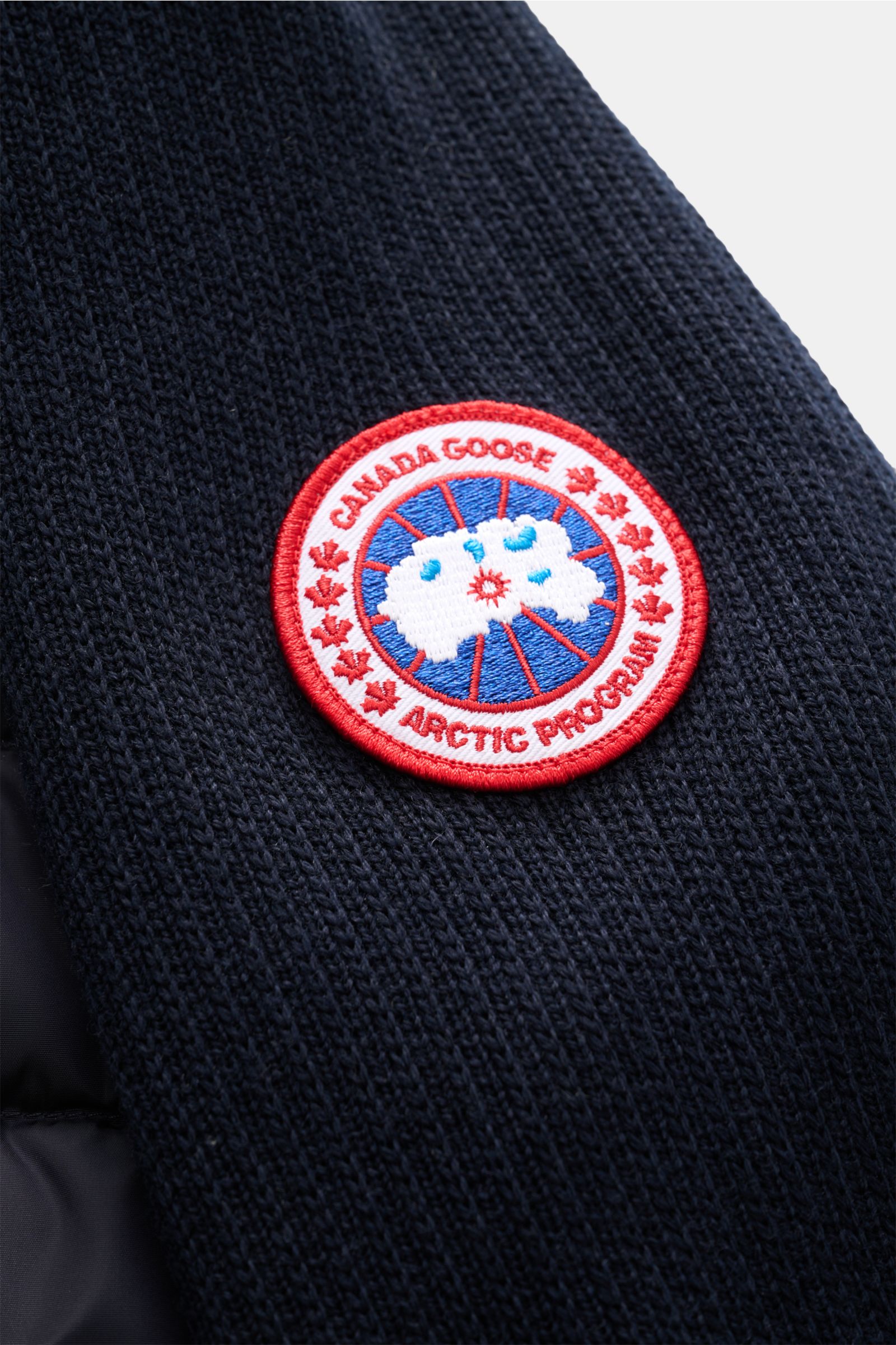 Nahaufnahme der Canada Goose Strickjacke 'Hybridge Knit' navy mit strukturiertem Wollstrick und rotem Markenlogo auf dem Oberarm, Detailansicht.