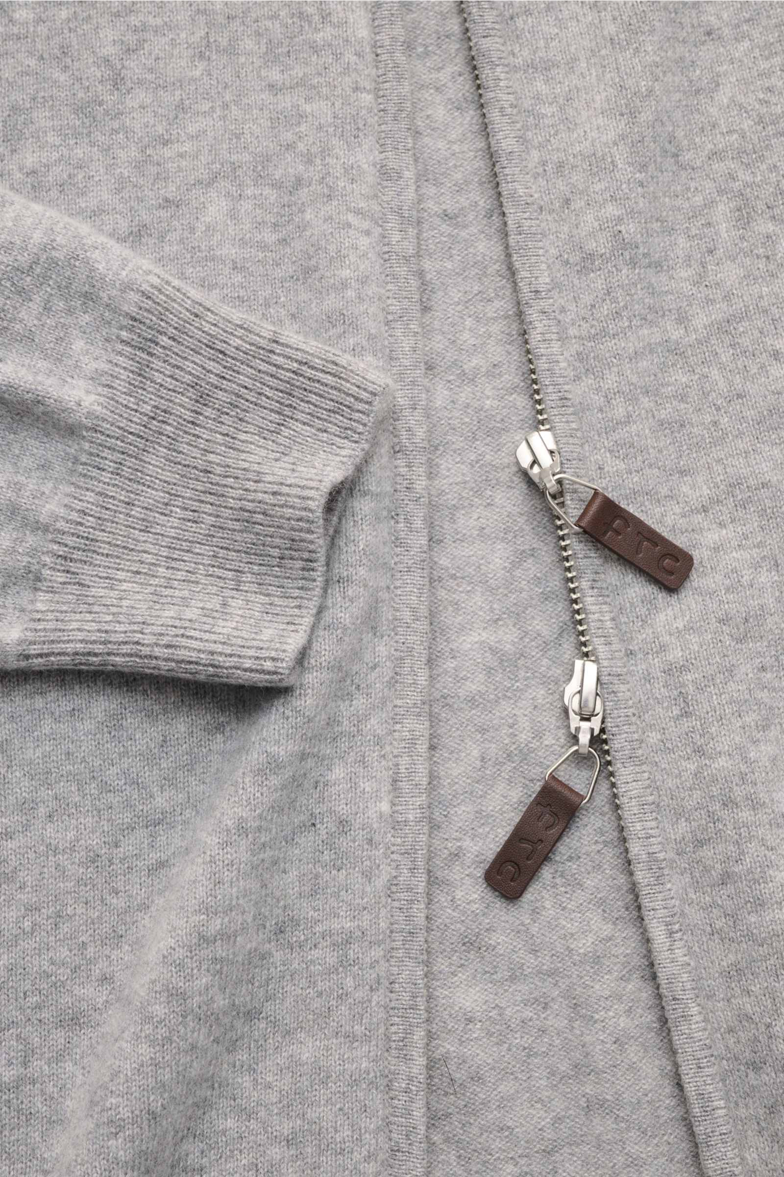 Nahaufnahme der FTC Cashmere Strickjacke grau meliert von oben, zeigt feines Strickbild, zwei-Wege-Reißverschluss mit Leder-Logo und gerippten Ärmelbündchen. Fair-Trade-Cashmere, OEKO-TEX® zertifiziert, sehr weich, Slim Fit, Stehkragen.