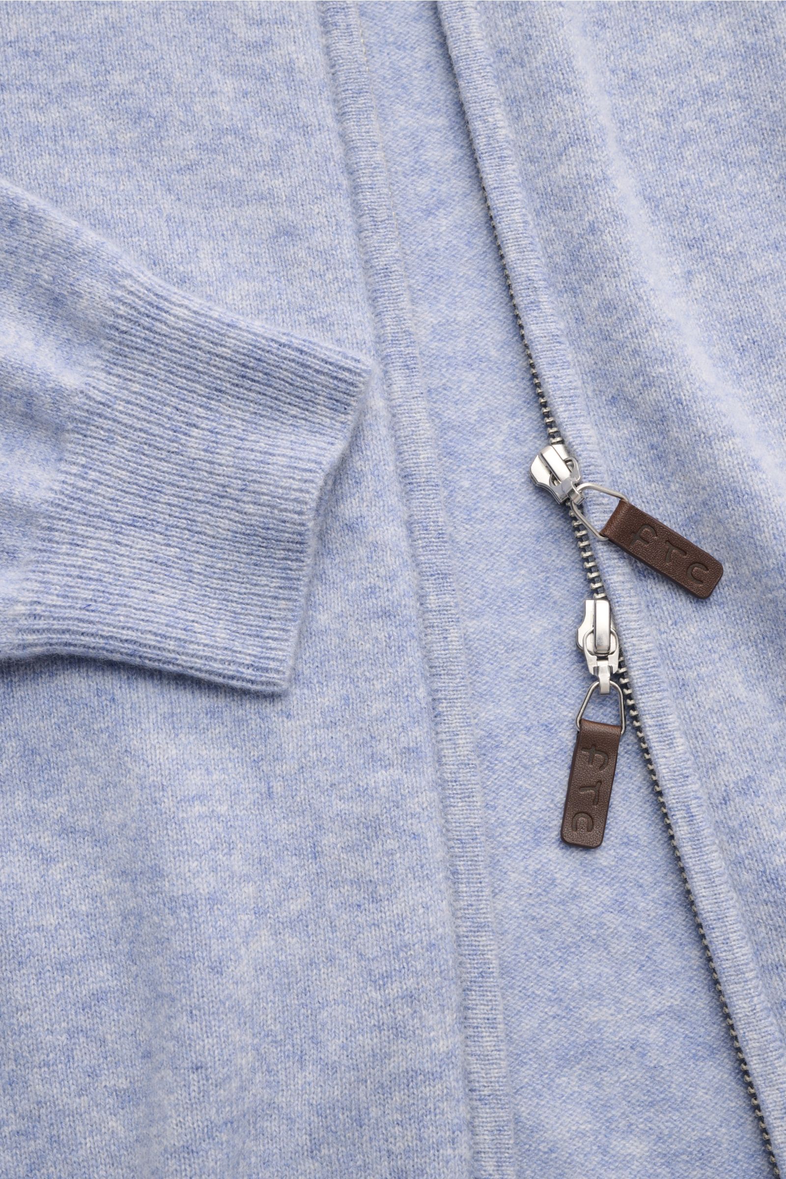 Nahaufnahme der hellblau melierten FTC Cashmere Strickjacke mit verdecktem Zwei-Wege-Reißverschluss, Leder-Logo am Zipper, geripptem Stehkragen und flexiblen Rippbündchen aus reinem Fair-Trade-Cashmere, OEKO-TEX® zertifiziert, feinem Strickbild und sehr w