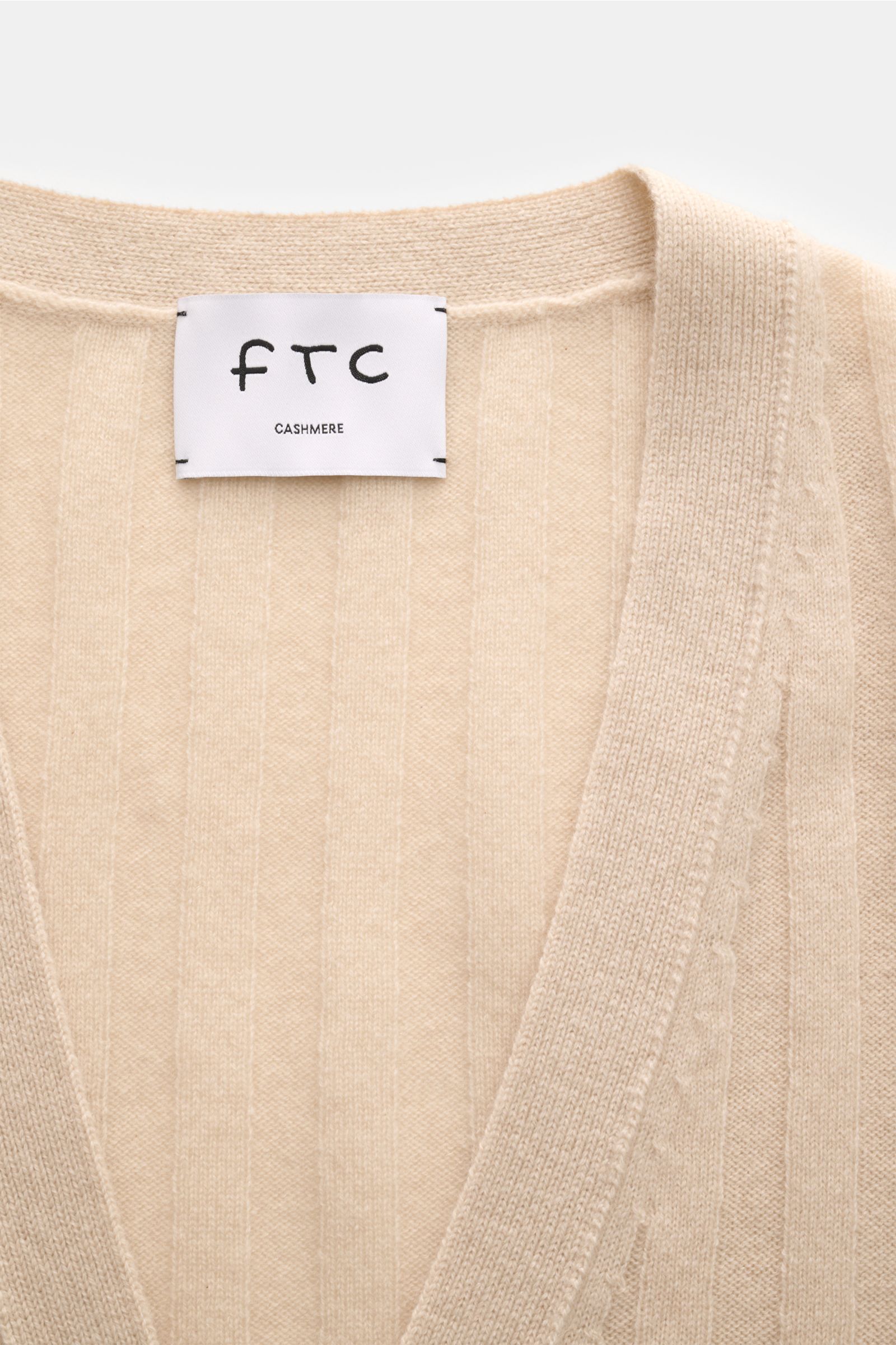 Nahaufnahme des FTC Cashmere Cardigan beige von oben, zeigt V-Ausschnitt, breiten Rippstrick, feines Strickbild, Vier-Knopf-Leiste, Fair-Trade-Cashmere.