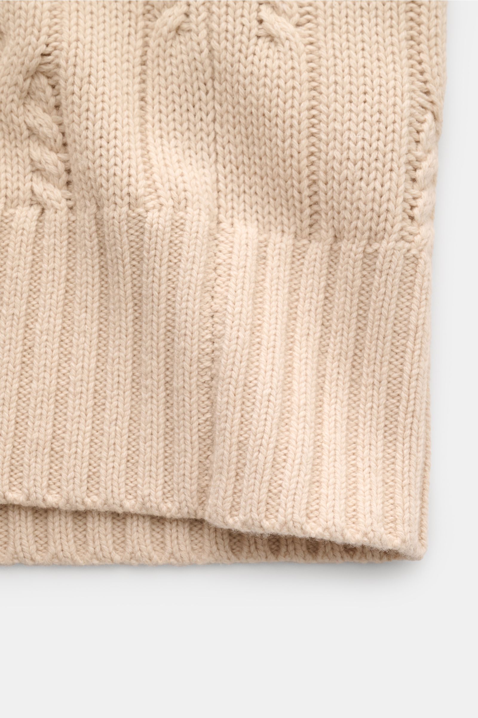 Nahaufnahme des FTC Cardigan beige am unteren Saum, zeigt den weichen Strick aus Bio-Baumwolle und Fair-Trade-Cashmere mit Zopfstrick, breiten Rippbündchen und mittelgrobem Strickbild, fotografiert von vorne unten.