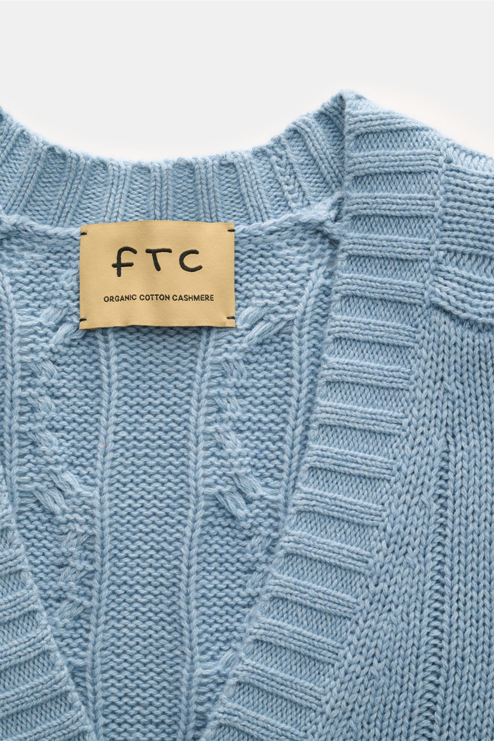 Nahaufnahme des FTC Cardigan hellblau mit Zopfstrick-Design, V-Ausschnitt und weichem, mittelgrobem Strick aus Bio-Baumwolle und Fair-Trade-Cashmere.
