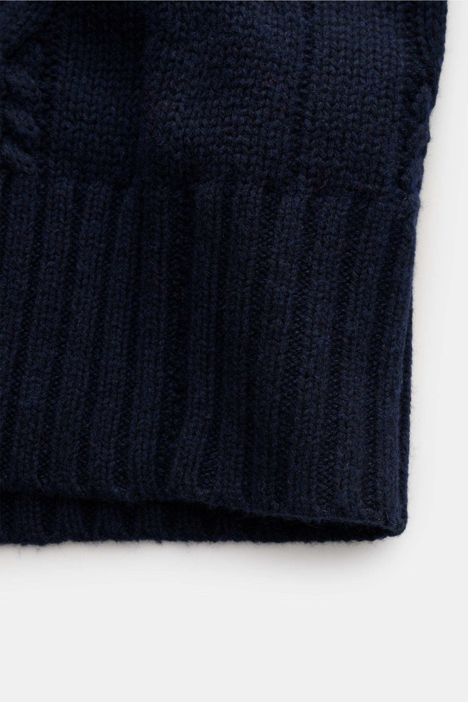Nahaufnahme des unteren Saums des FTC Cardigan navy mit breiten Rippbündchen und mittelgrobem, weichem Zopfstrick aus Bio-Baumwolle und Fair-Trade-Cashmere, fotografiert von vorne.