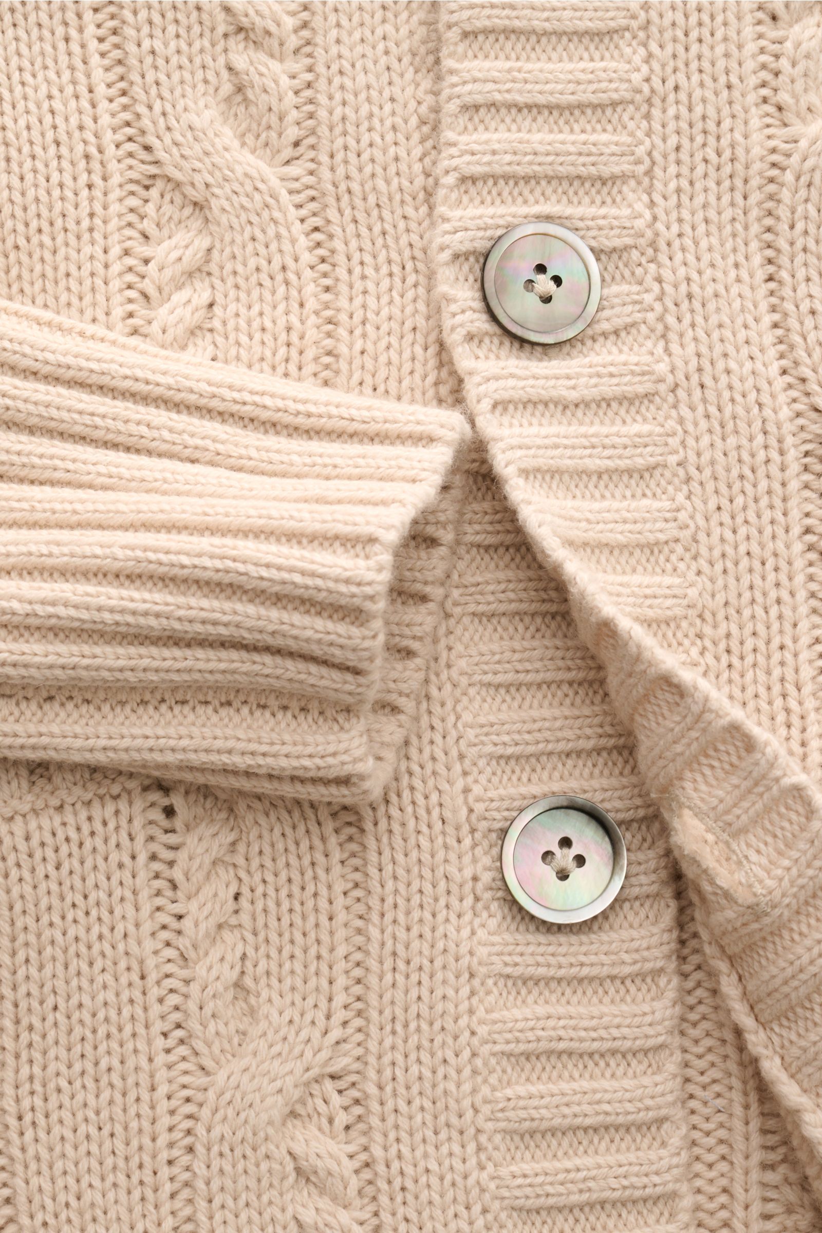 Nahaufnahme des FTC Cardigan beige aus Bio-Baumwolle und Fair-Trade-Cashmere, zeigt Zopfstrick, Knöpfe, Rippbündchen und Leistentaschen.