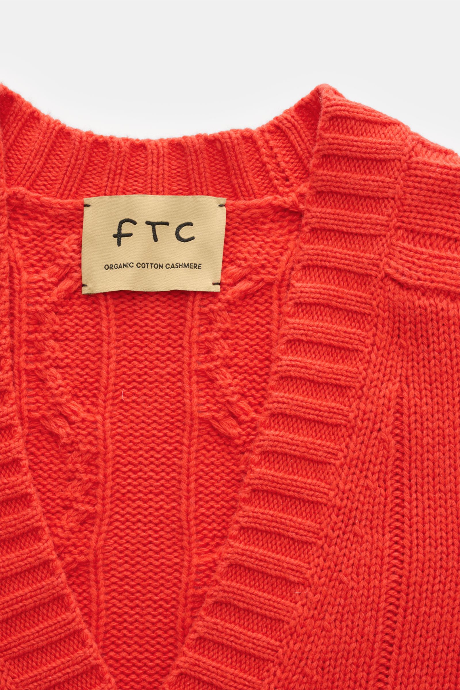 Nahaufnahme des FTC Cardigan hellrot von oben, zeigt V-Ausschnitt, Zopfstrick-Design, breite Rippbündchen, Bio-Baumwolle und Fair-Trade-Cashmere.