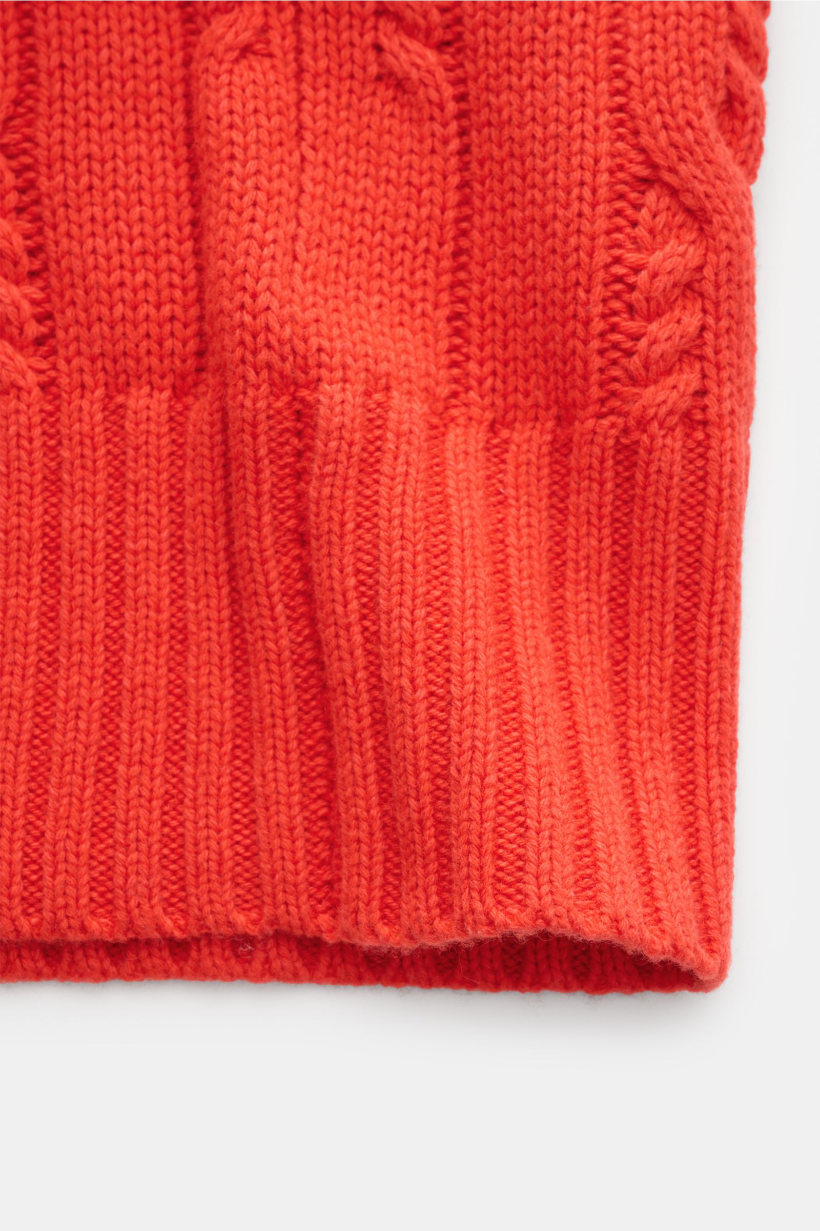 Nahaufnahme des unteren Bereichs des FTC Cardigan hellrot, gestrickt aus Bio-Baumwolle und Fair-Trade-Cashmere mit Zopfstrick-Design, breiten Rippbündchen und mittelgrobem Strickbild.