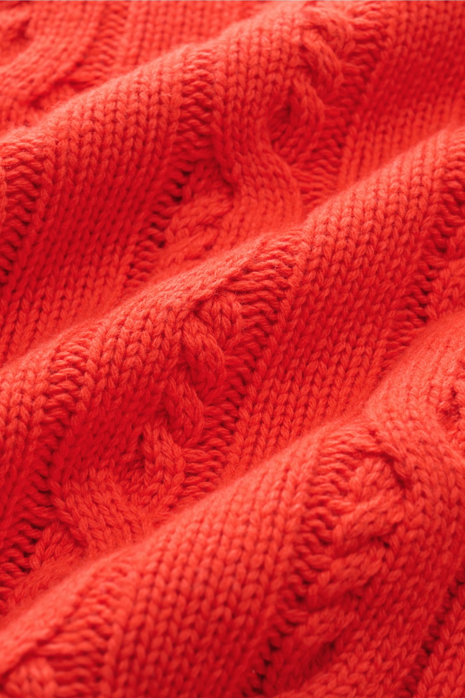 Nahaufnahme des hellroten FTC Cardigan mit Zopfstrick-Design aus Bio-Baumwolle und Fair-Trade-Cashmere, weicher Griff, mittelgrobes Strickbild.