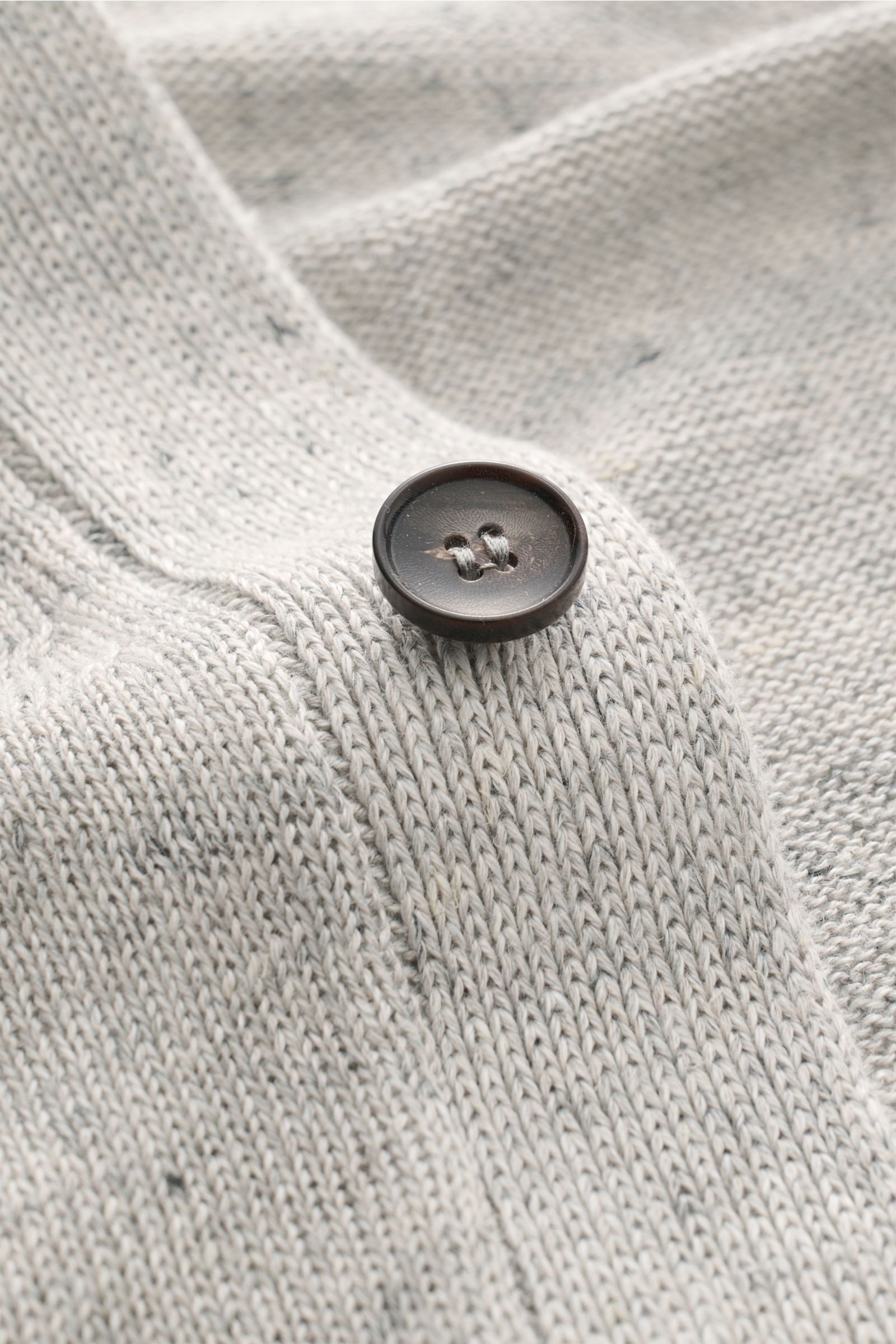 Close-up front view of a dark brown button on the light grey textured knit fabric of the Filippo de Laurentiis Cardigan grau meliert. Stylisch ohne viel Aufwand: Mit seinem leichten Materialmix aus Leinen und Baumwolle wird der Cardigan von FILIPPO DE LAU