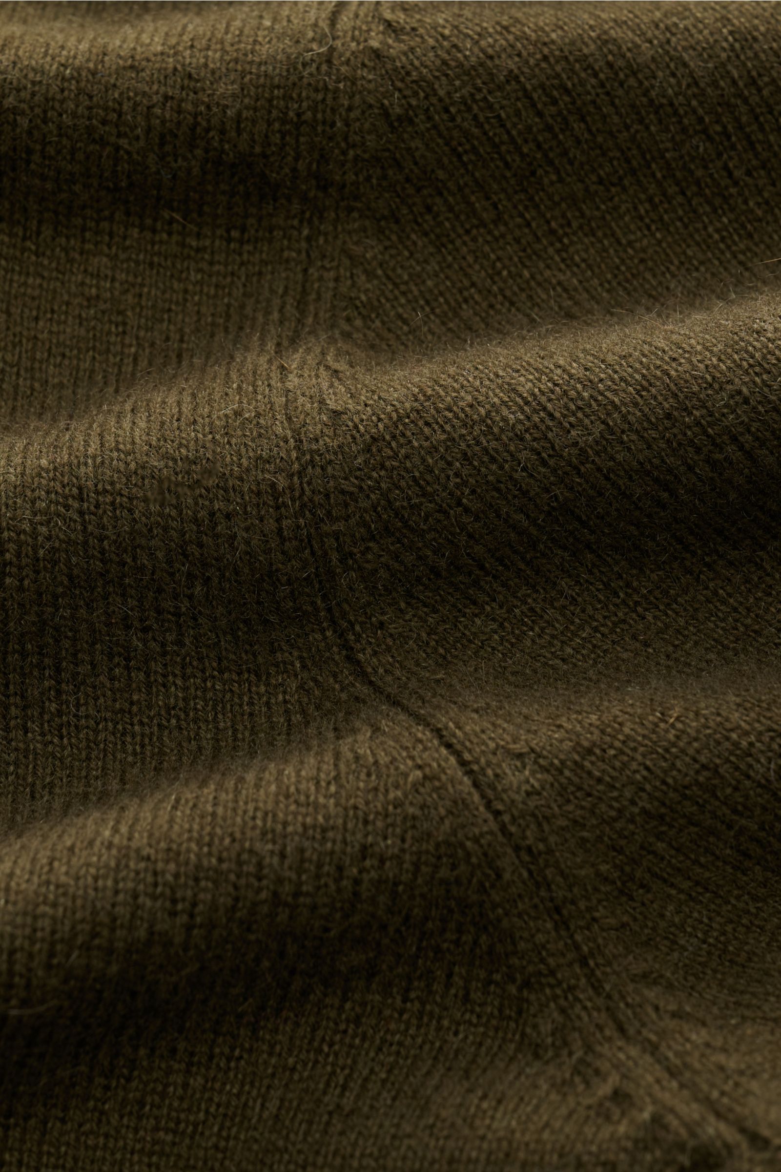 Nahaufnahme der von Braun Cashmere Strickjacke dark olive aus mongolischem Cashmere mit feinem Strickbild, Slim Fit, Reißverschluss, Stehkragen und Rippbündchen, fotografiert aus seitlicher Perspektive.