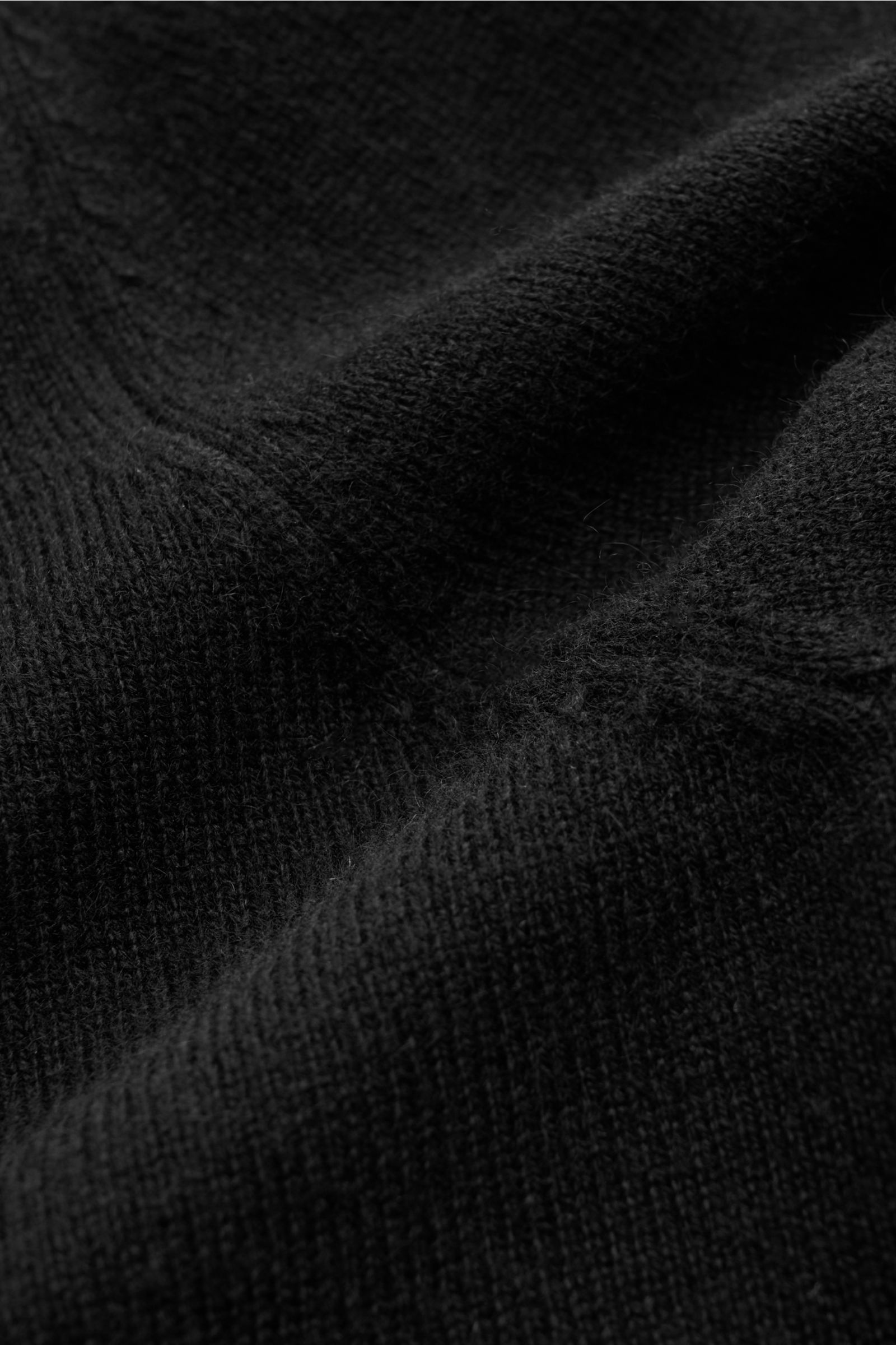 Nahaufnahme der von Braun Cashmere Strickjacke schwarz aus mongolischem Cashmere, fein gestrickt mit weichem Griff, Slim Fit, Reißverschluss, Stehkragen und Rippbündchen, fotografiert aus schräger Perspektive.