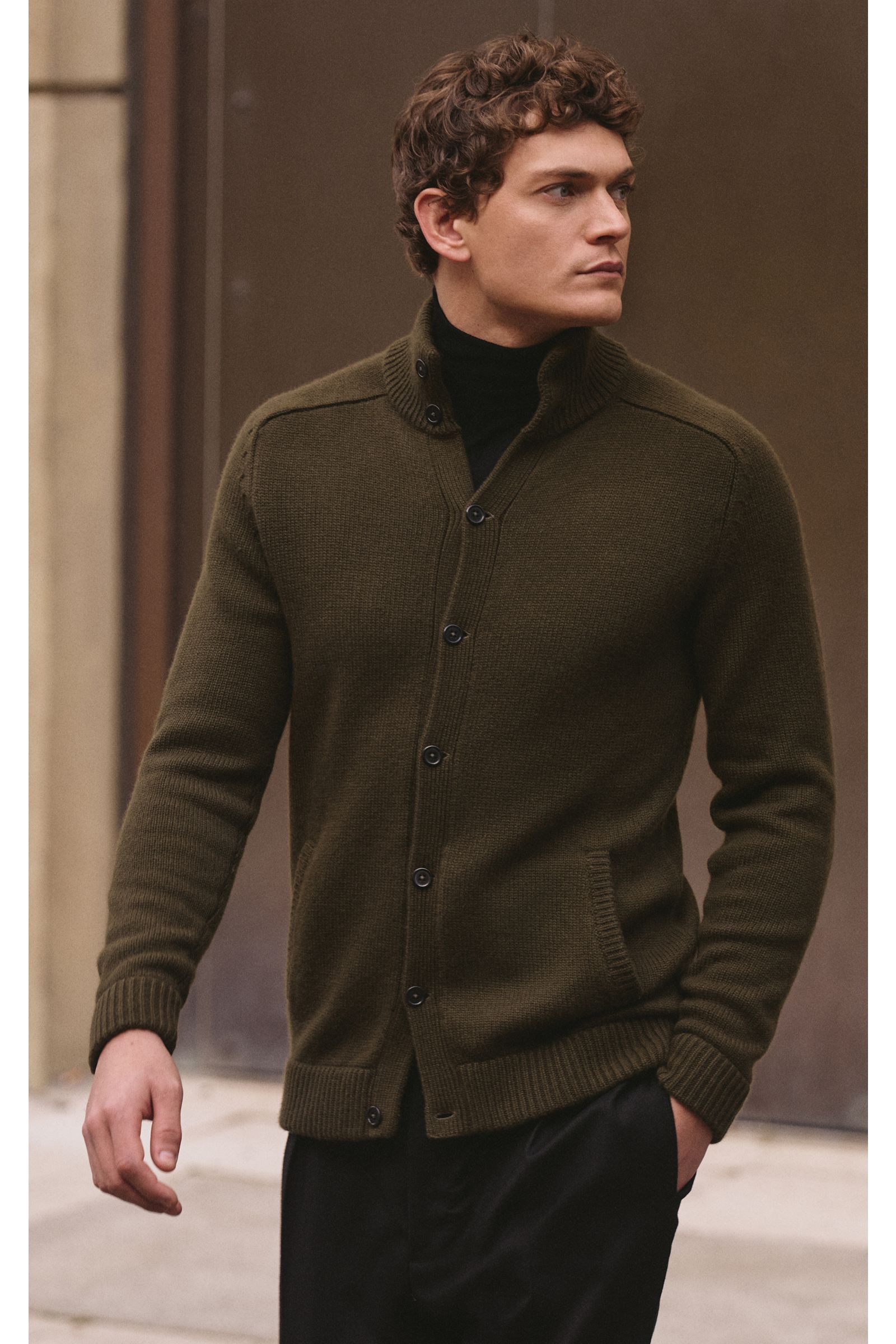 Mann von vorn seitlich fotografiert trägt von Braun Cashmere Cardigan oliv aus reinem mongolischem Cashmere mit Stehkragen, Knopfleiste, Taschen.